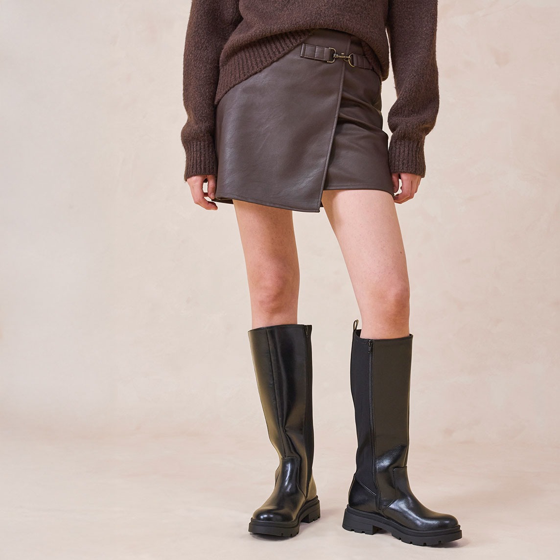 Lederrock und kniehohe Stiefel kombiniert mit einem braunen Pullover.