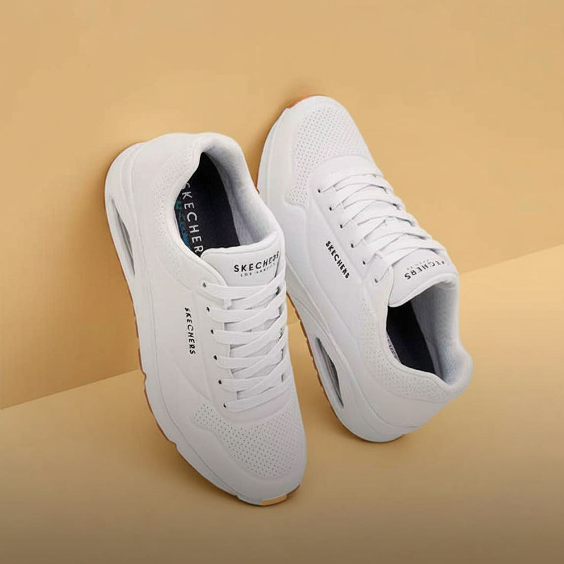 Weiße Sneaker mit perforierten Details und weißen Schnürsenkeln auf beigem Hintergrund präsentiert.