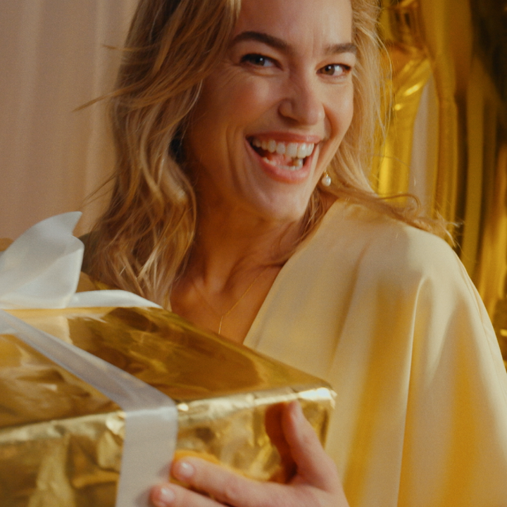 Eine Frau trägt ein gelbes Kleid und hält ein goldenes Geschenk.