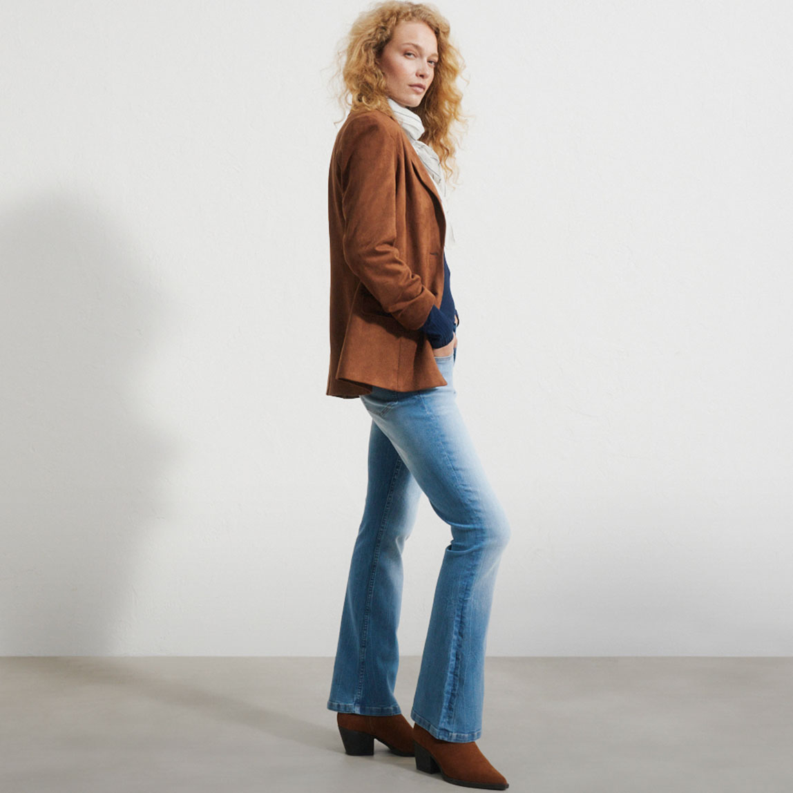Braune Wildlederjacke, lässige Schlagjeans, weißer Rollkragen und braune Stiefeletten.