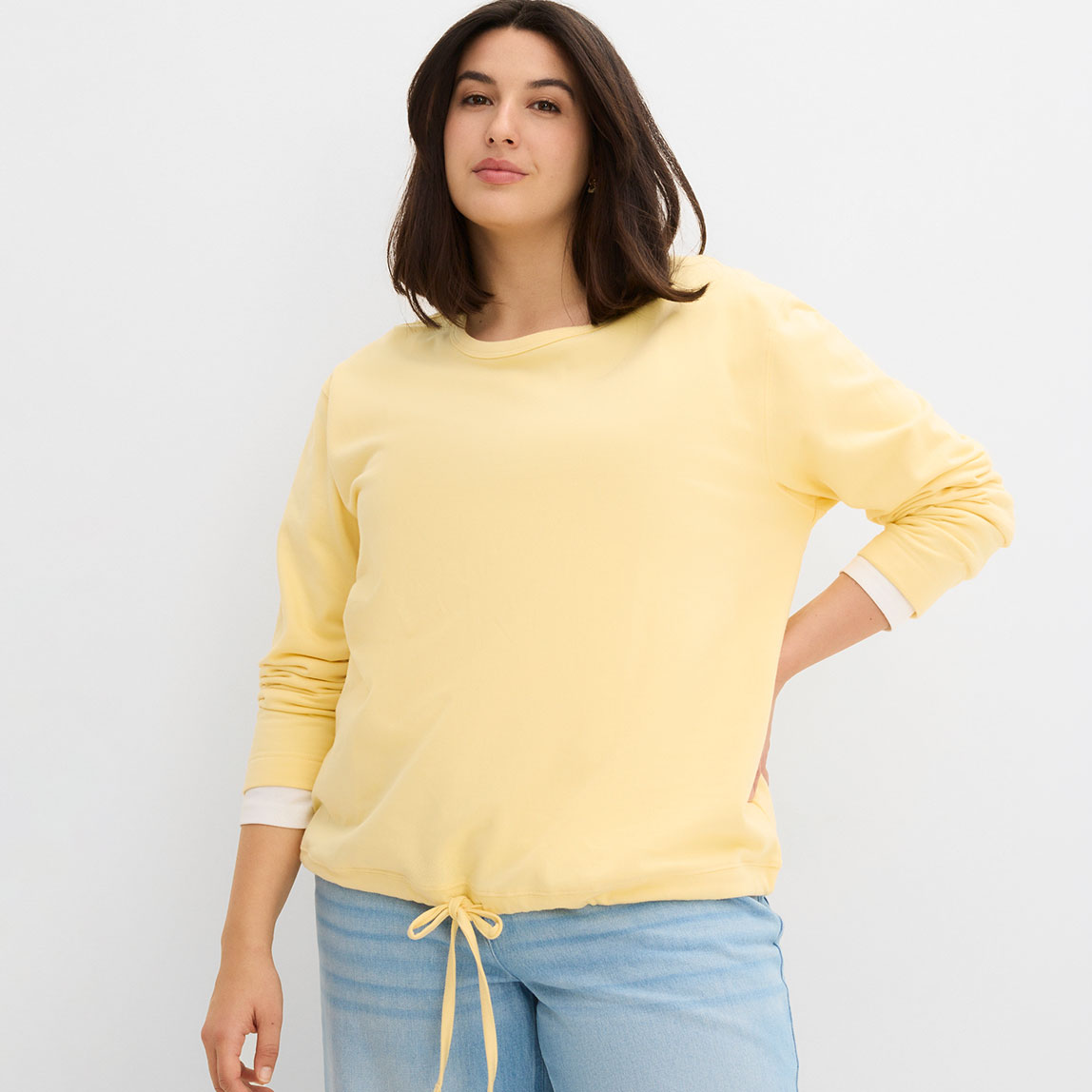 Gelbes Sweatshirt mit Kordelzug, kombiniert mit hellblauer Hose.