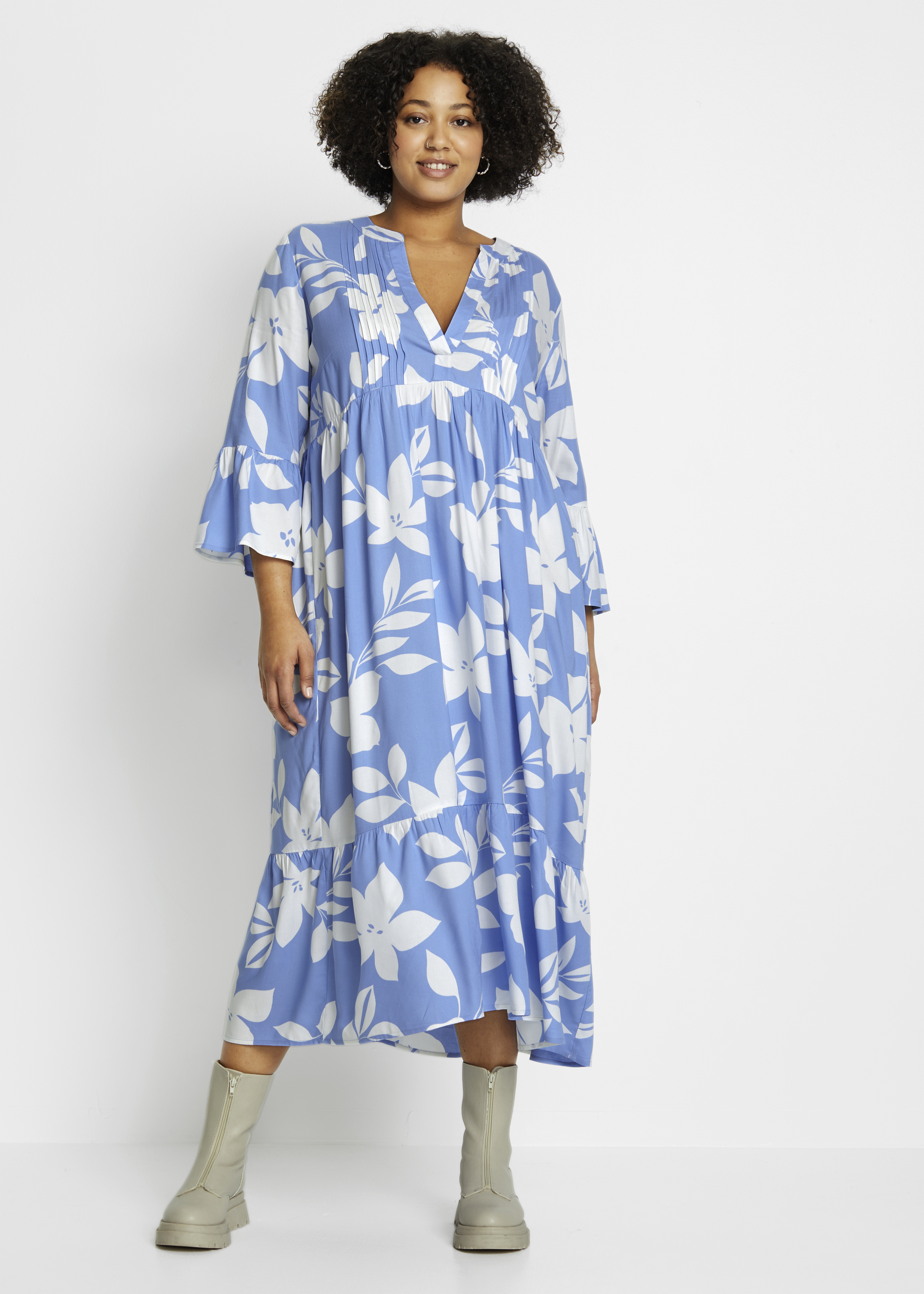 Luftiges, blaues Blumenkleid mit V-Ausschnitt, Glockenärmeln und Volant, dazu helle Stiefel.