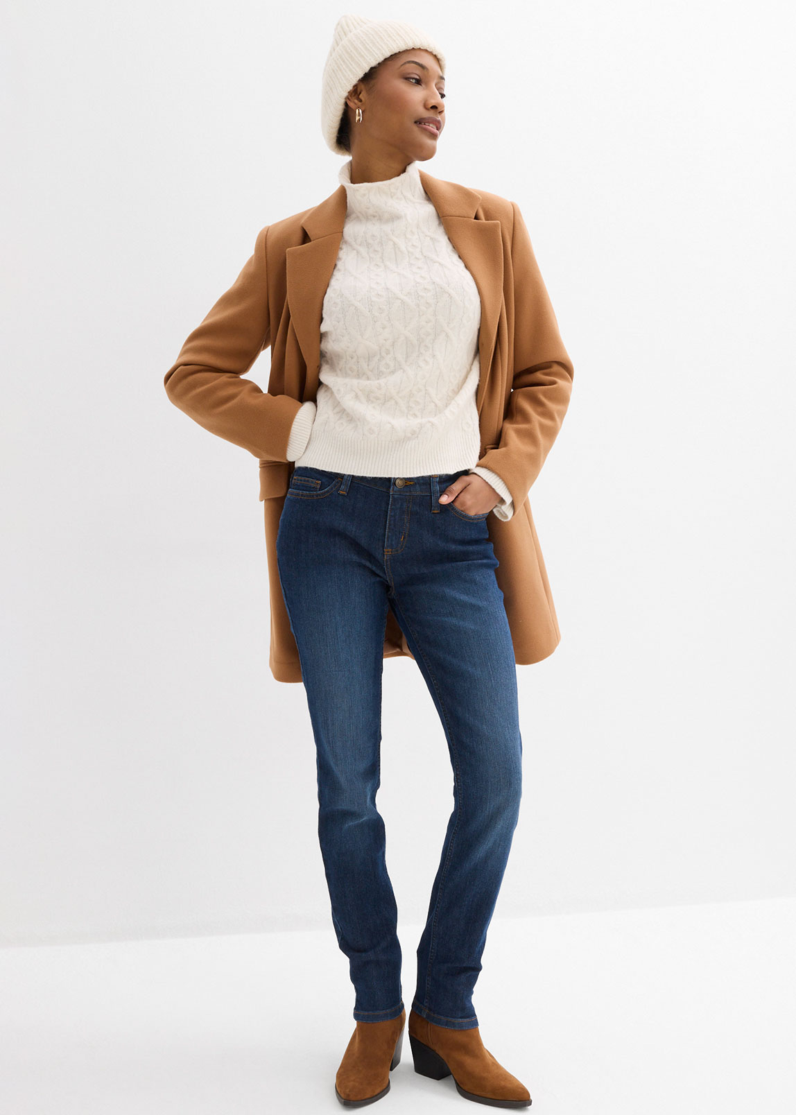Brauner Mantel, weißer Pullover, blaue Jeans und Mütze.