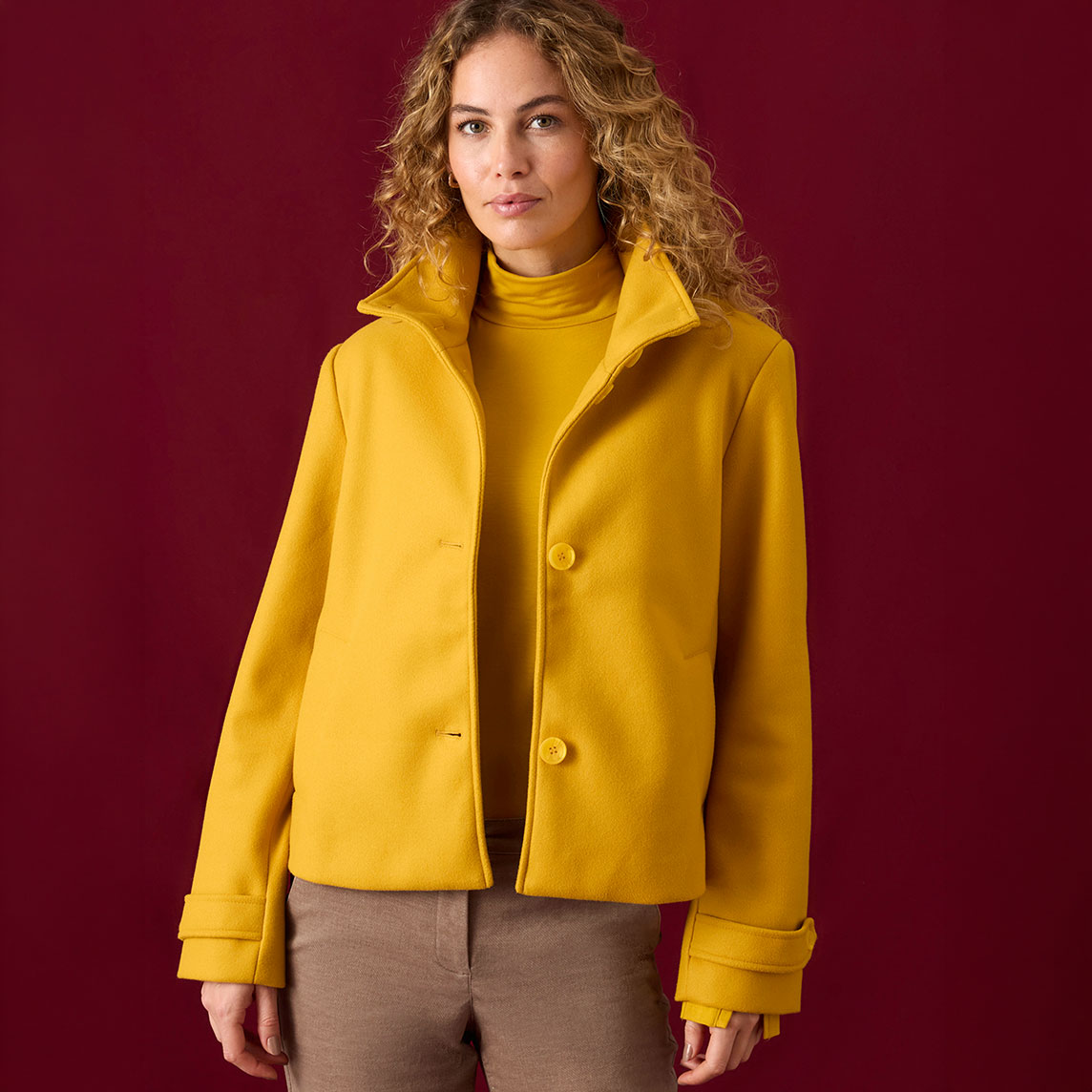 Gelber Mantel über Rollkragenpullover, kombiniert mit eleganter brauner Hose.