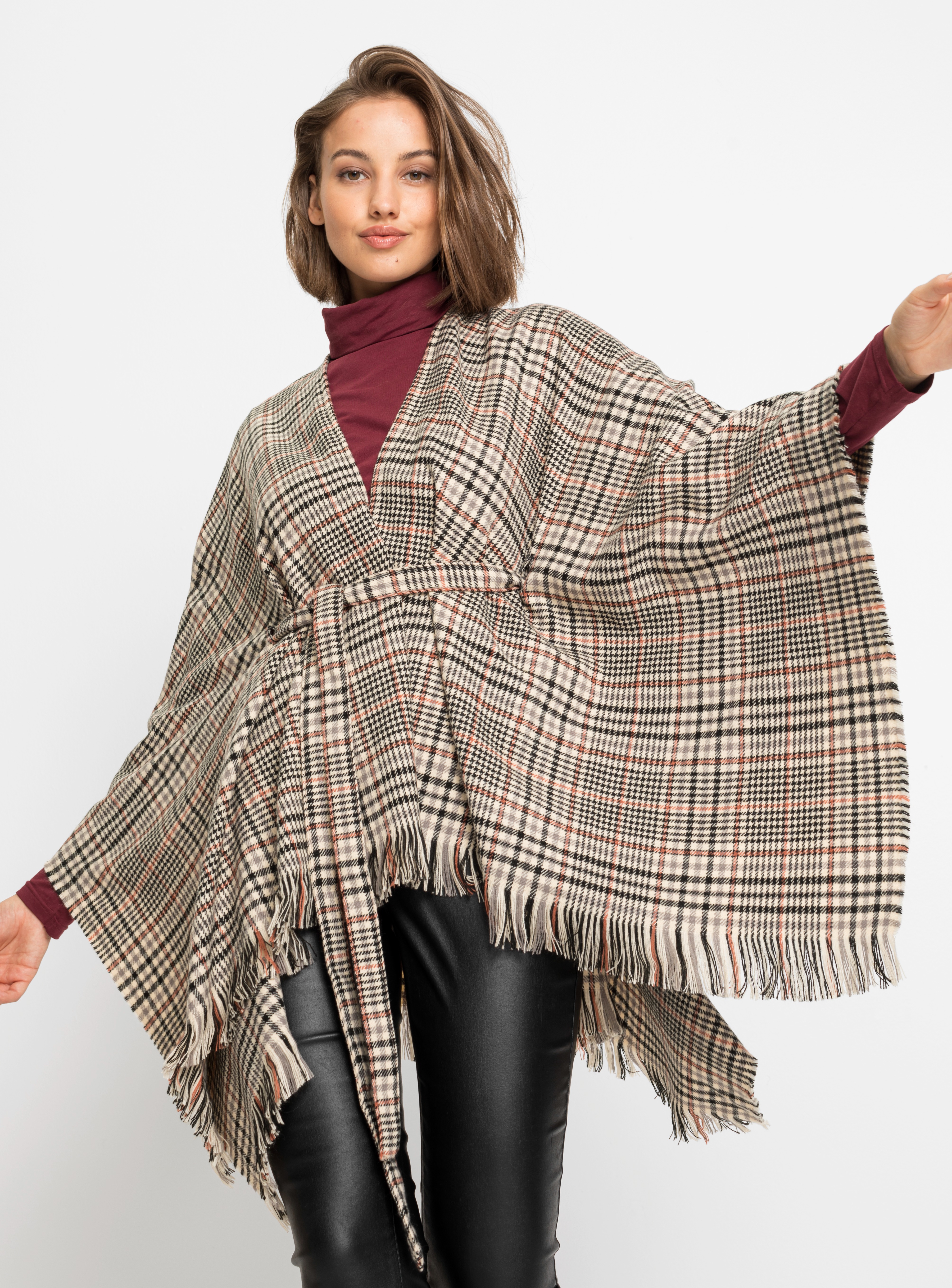 Karierter Poncho mit Fransen über weinrotem Rollkragenpullover.