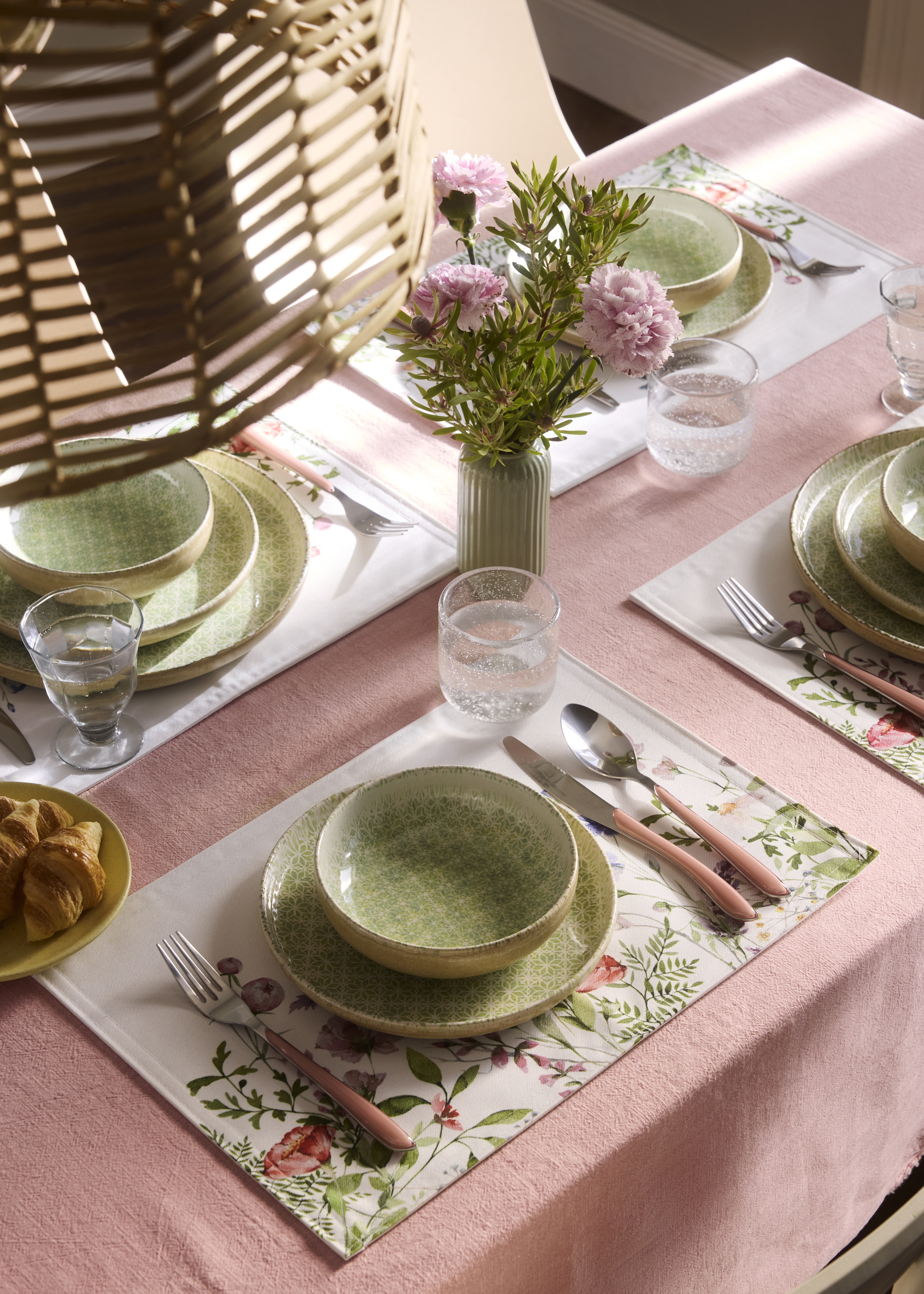 Tisch mit rosa Tischdecke, Platzsets und zarten grünen Tellern.