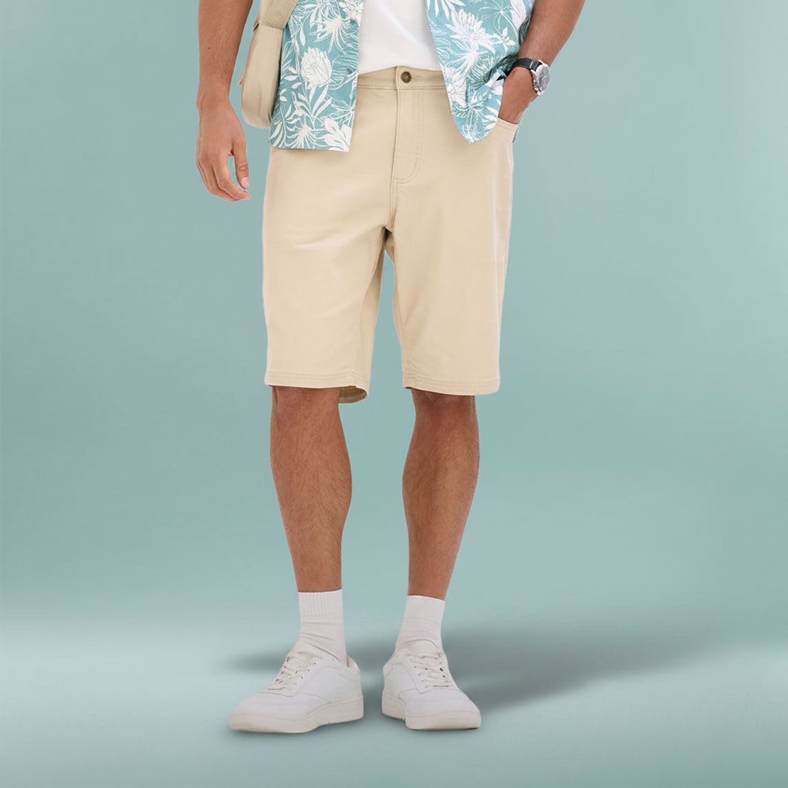 Lässiges Sommeroutfit mit beiger Bermuda-Shorts, gemustertem Hemd und weißen Sneakers.