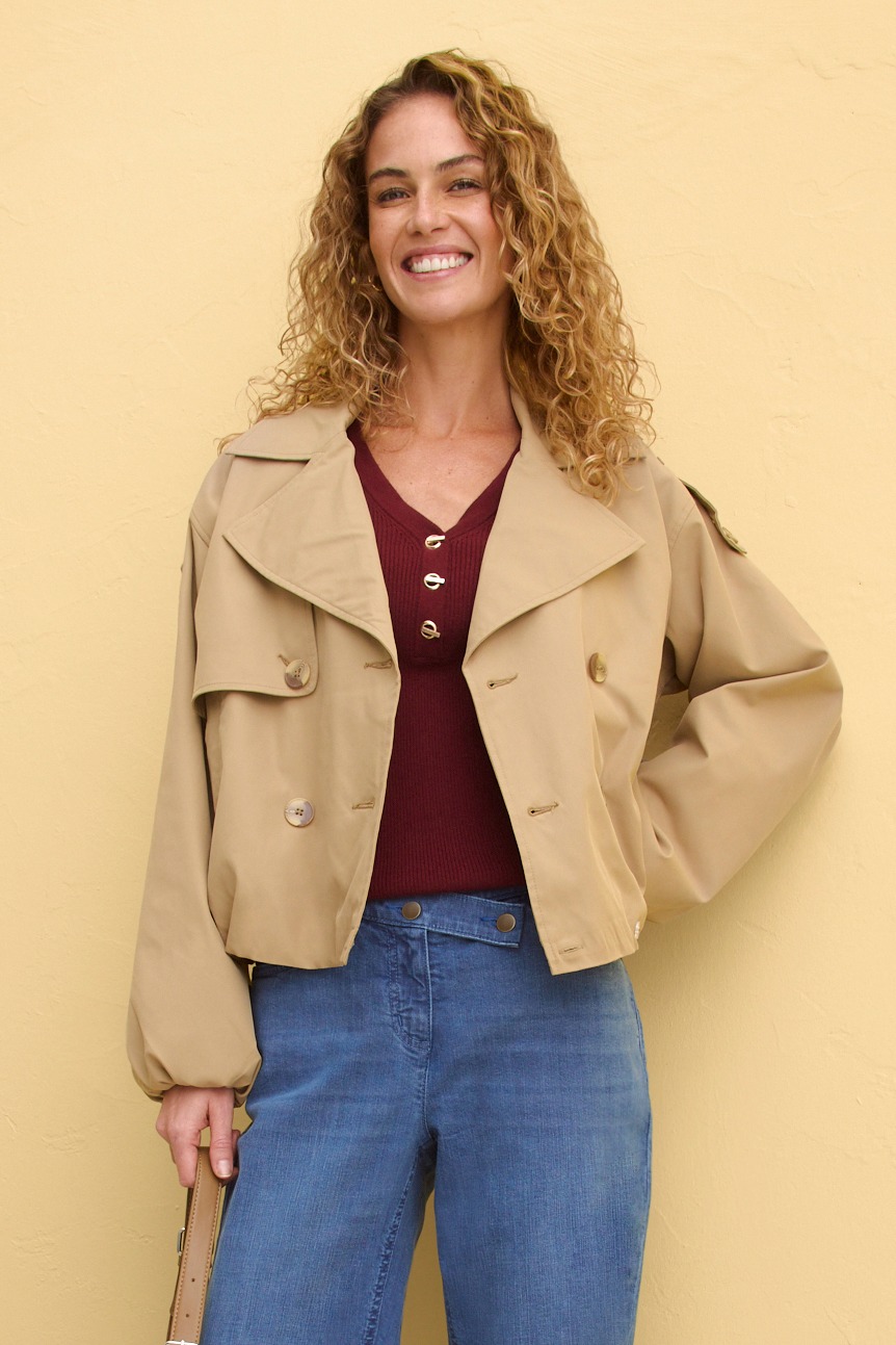 Beiger Kurzmantel über weinrotem Oberteil, kombiniert mit blauer Jeans.