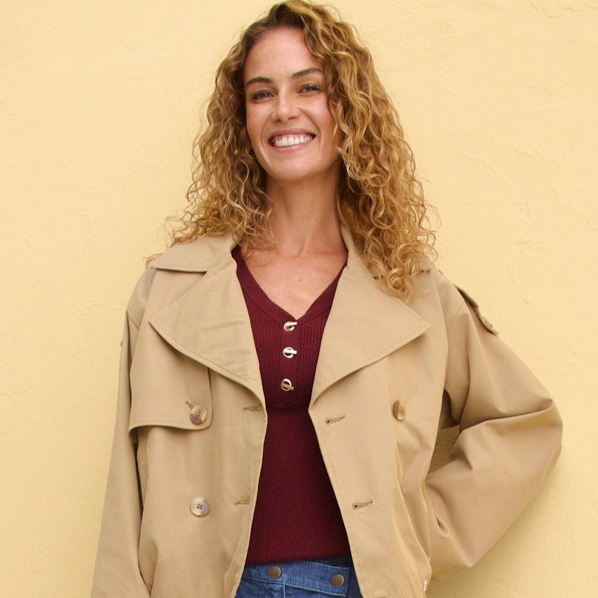 Beiger Kurzmantel über weinrotem Oberteil, kombiniert mit blauer Jeans.