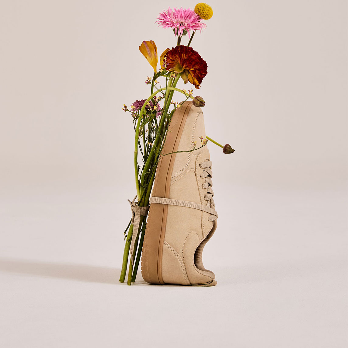 Elegante schwarze Sandalen, daneben eine Vase mit roten Blumen.