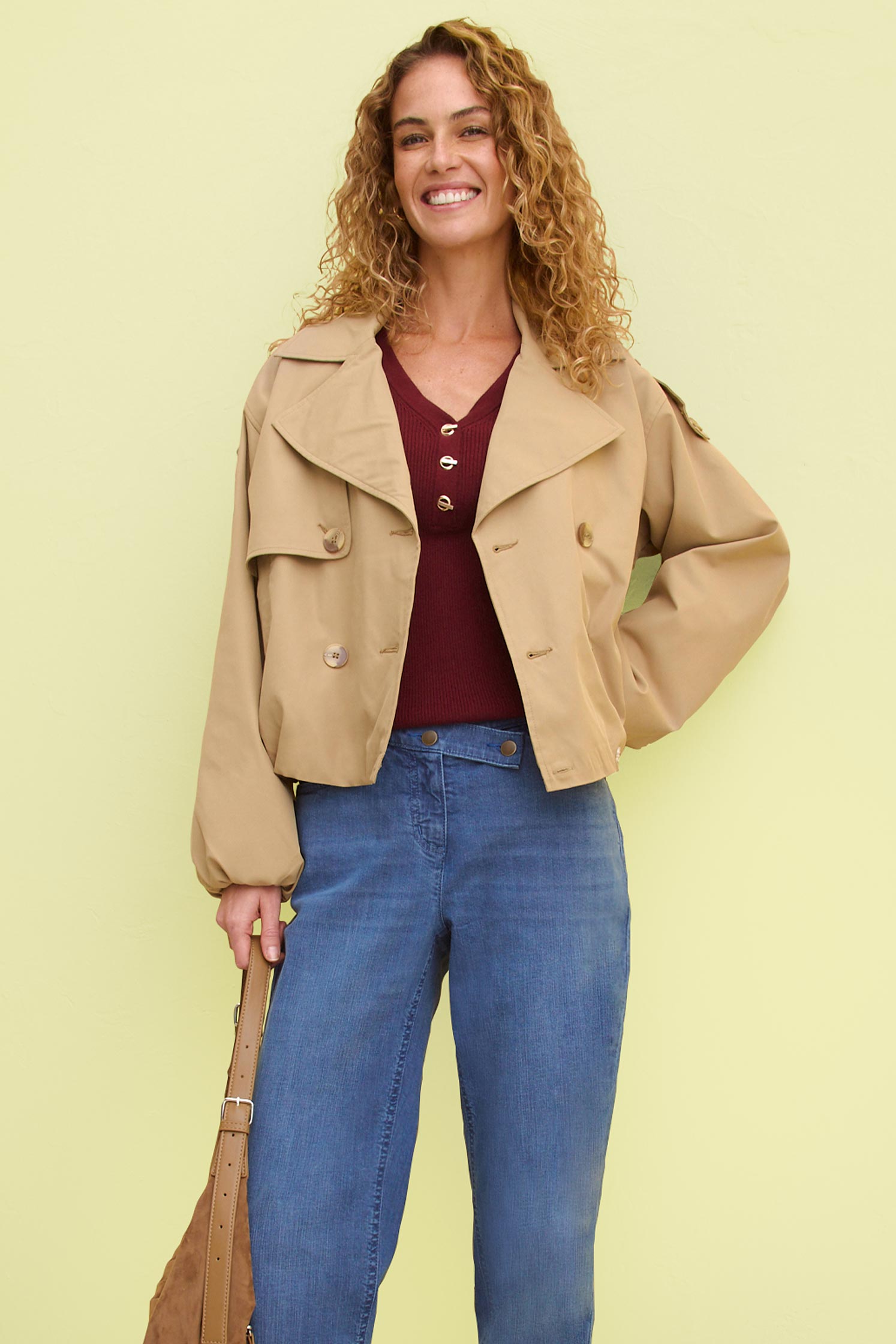 Beige Jacke über weinrotem Oberteil, blaue Jeans und braune Tasche.