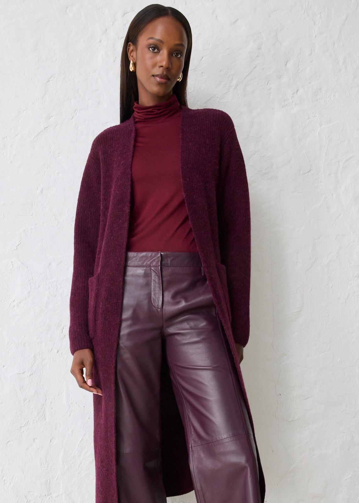 Langer Cardigan, Rollkragenpullover und Lederhose in harmonischen Weinrot- und Lilatönen.