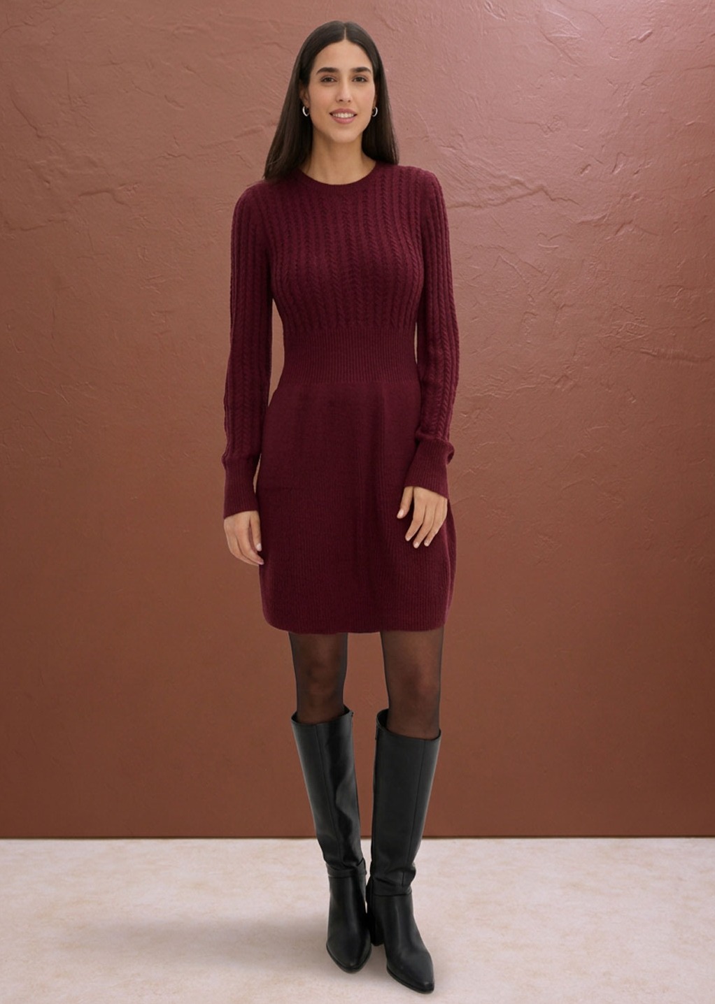 Elegantes Strickkleid in Bordeaux, kombiniert mit schwarzen Strümpfen und hohen Stiefeln.