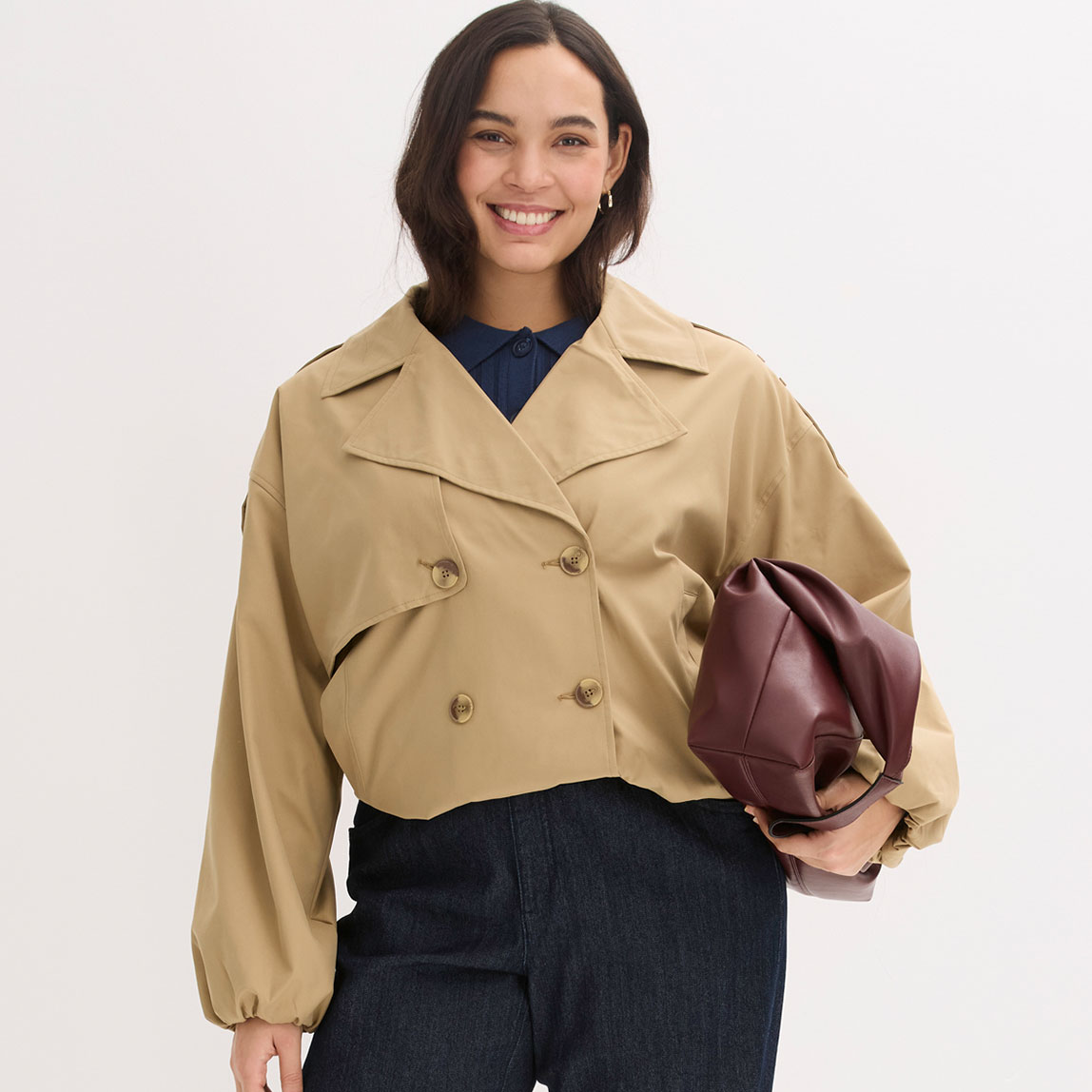 Beige Trenchjacke über dunklem Oberteil. Dazu eine braune Handtasche.