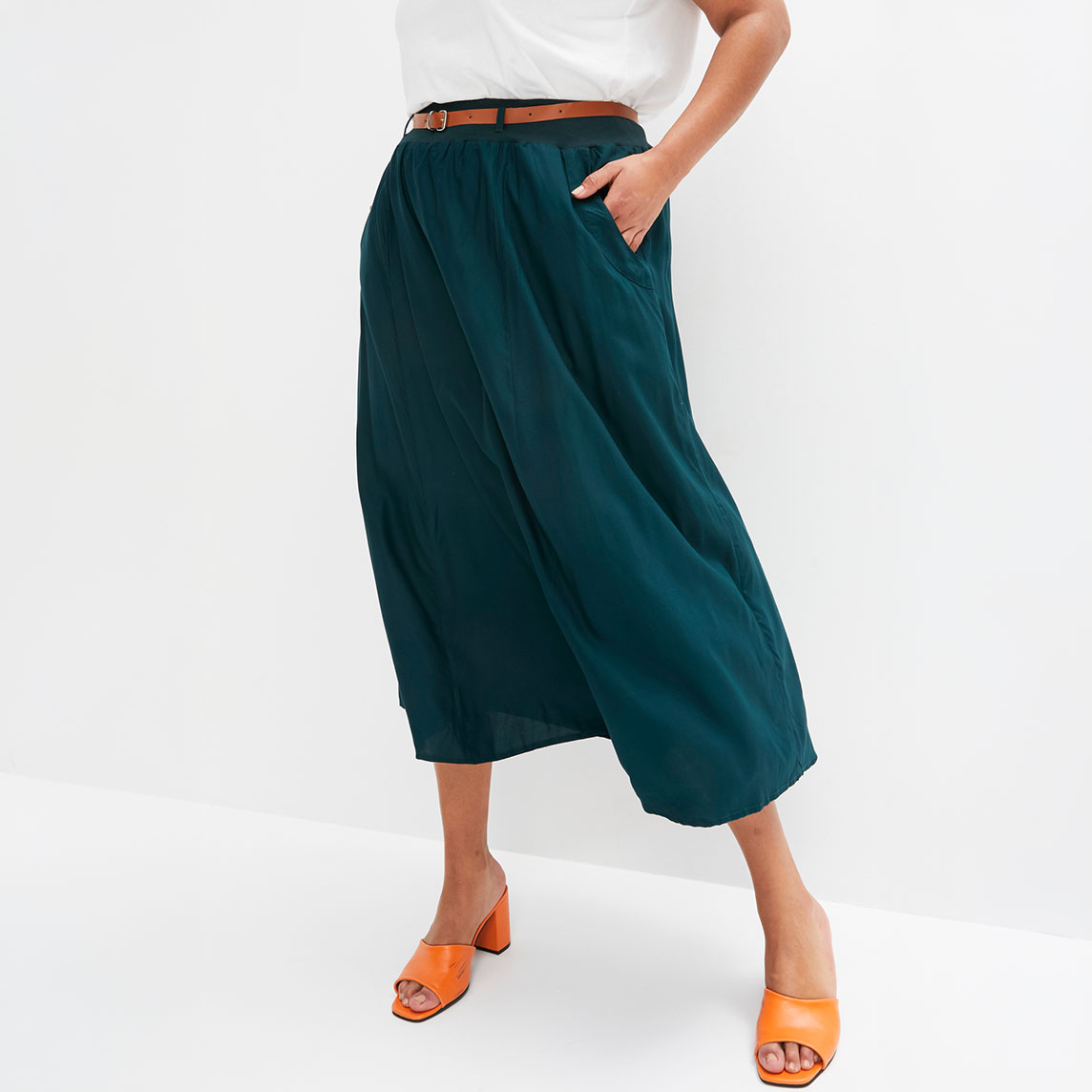 Eleganter petrolblauer Rock mit braunem Gürtel, weißem Oberteil und orangefarbenen Sandalen.