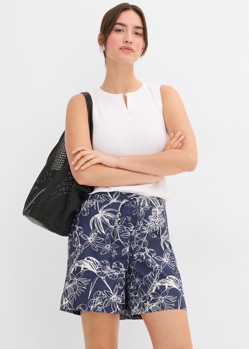 Weiße ärmellose Bluse, dunkelblaue Shorts mit Blumenmuster und schwarze perforierte Tasche.