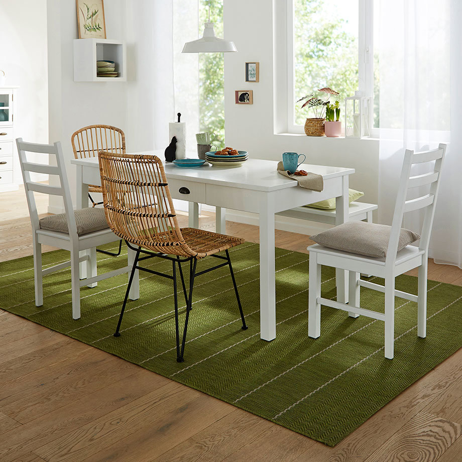 Moderner Esszimmerstuhl aus Rattan kontrastiert mit klassischen weißen Holzstühlen am schlichten Esstisch.