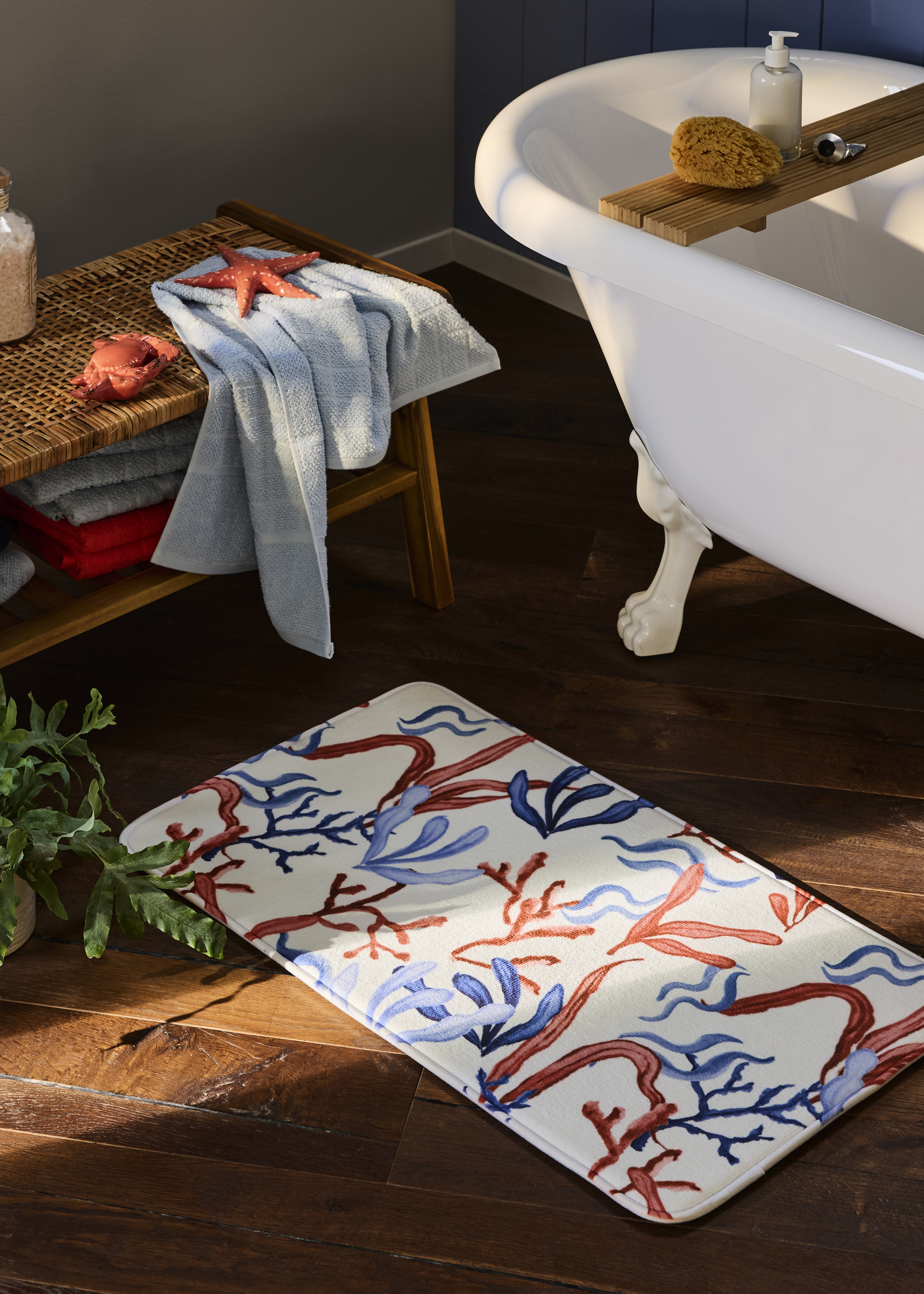 Ein hellblaues Handtuch liegt auf einer Holzbank neben einer freistehenden Badewanne.