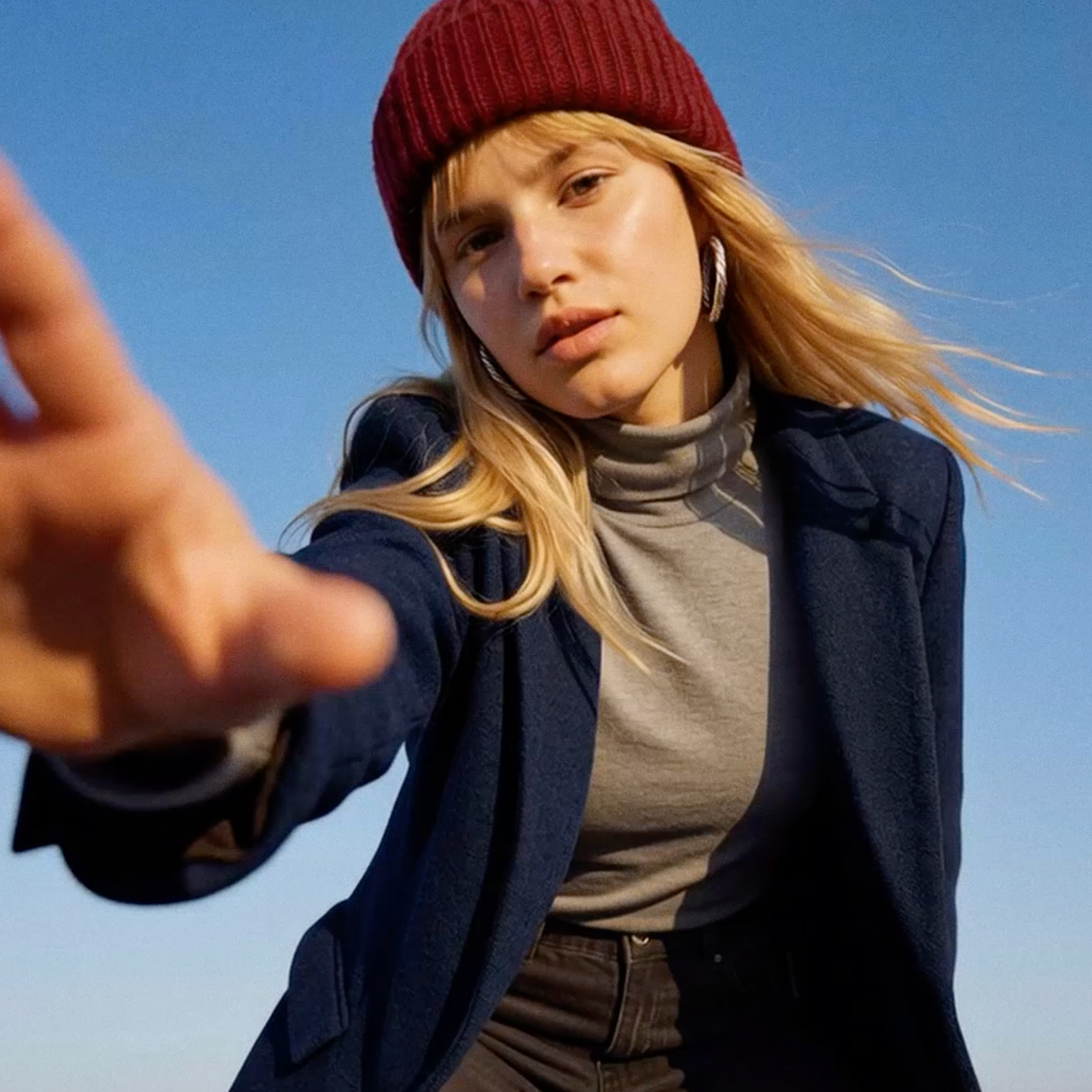 Rote Strickmütze, grauer Rollkragenpullover und dunkelblauer Blazer.