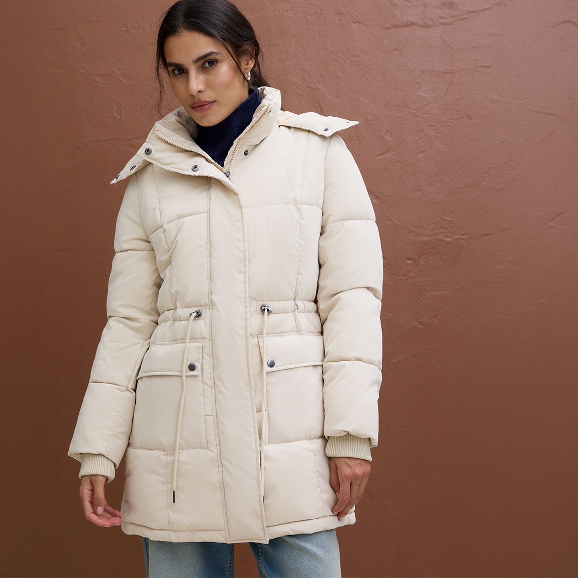 Modische, cremefarbene Steppjacke über dunklem Rollkragenpullover und heller Jeans.