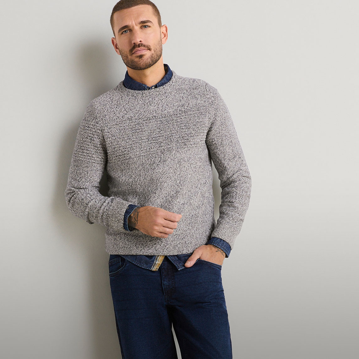 Stylischer, grober Strickpullover, Hemd darunter, kombiniert mit dunklen Jeans.