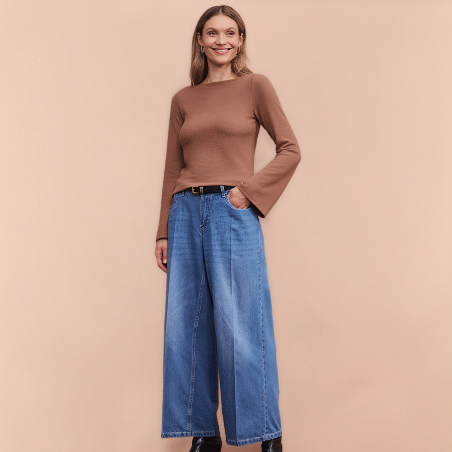 Weite Jeans und brauner Pullover mit Trompetenärmeln, dazu schwarze Stiefeletten.