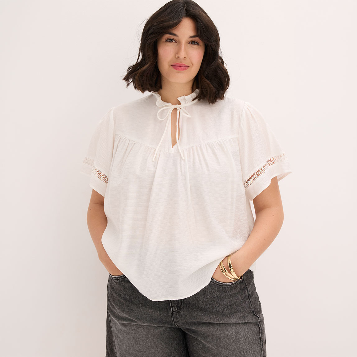 Weiße Bluse mit Rüschen, Bindeband und Spitzenärmeln.