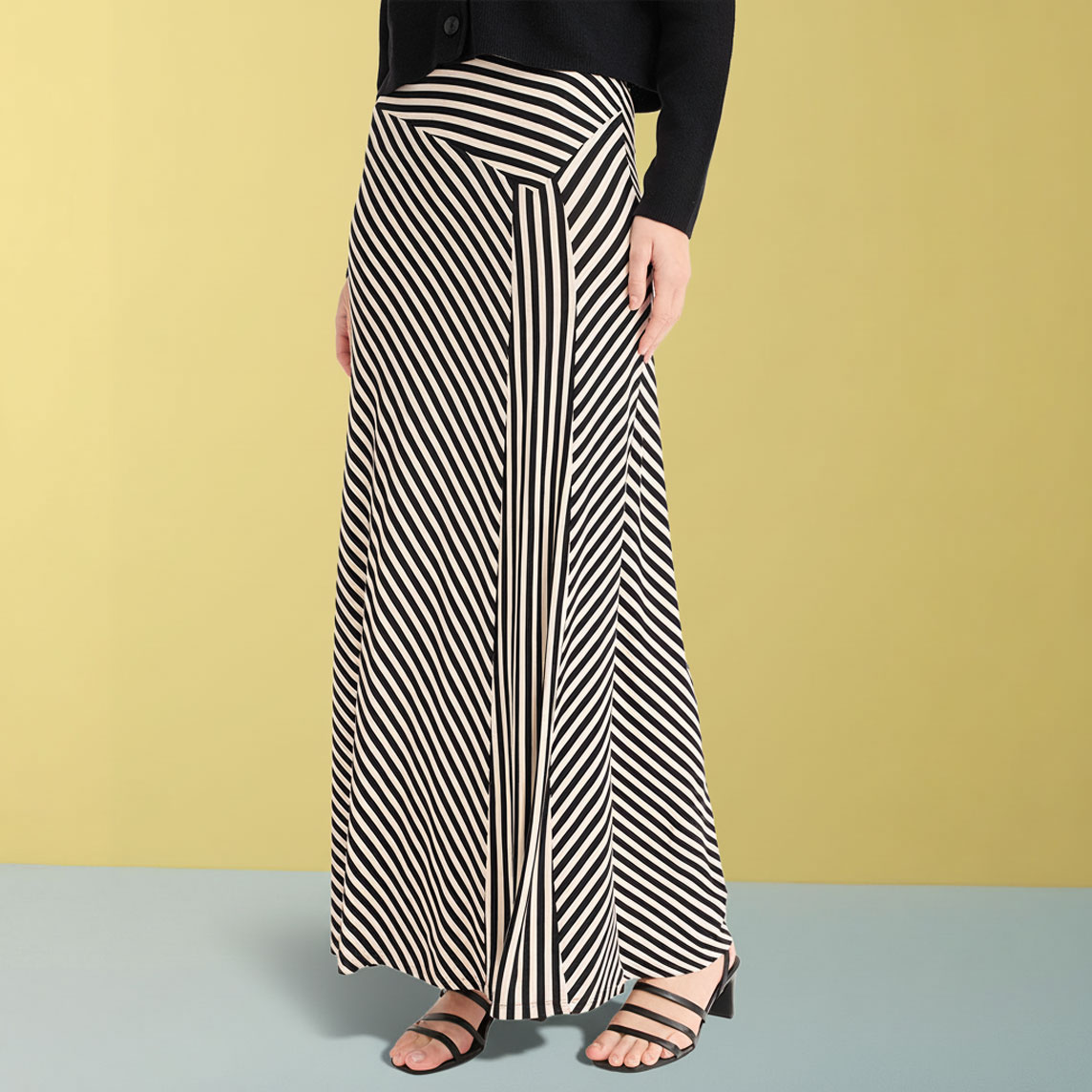 Eleganter Maxirock mit schwarz-weißen Streifen kombiniert mit schwarzem Oberteil und Sandalen.