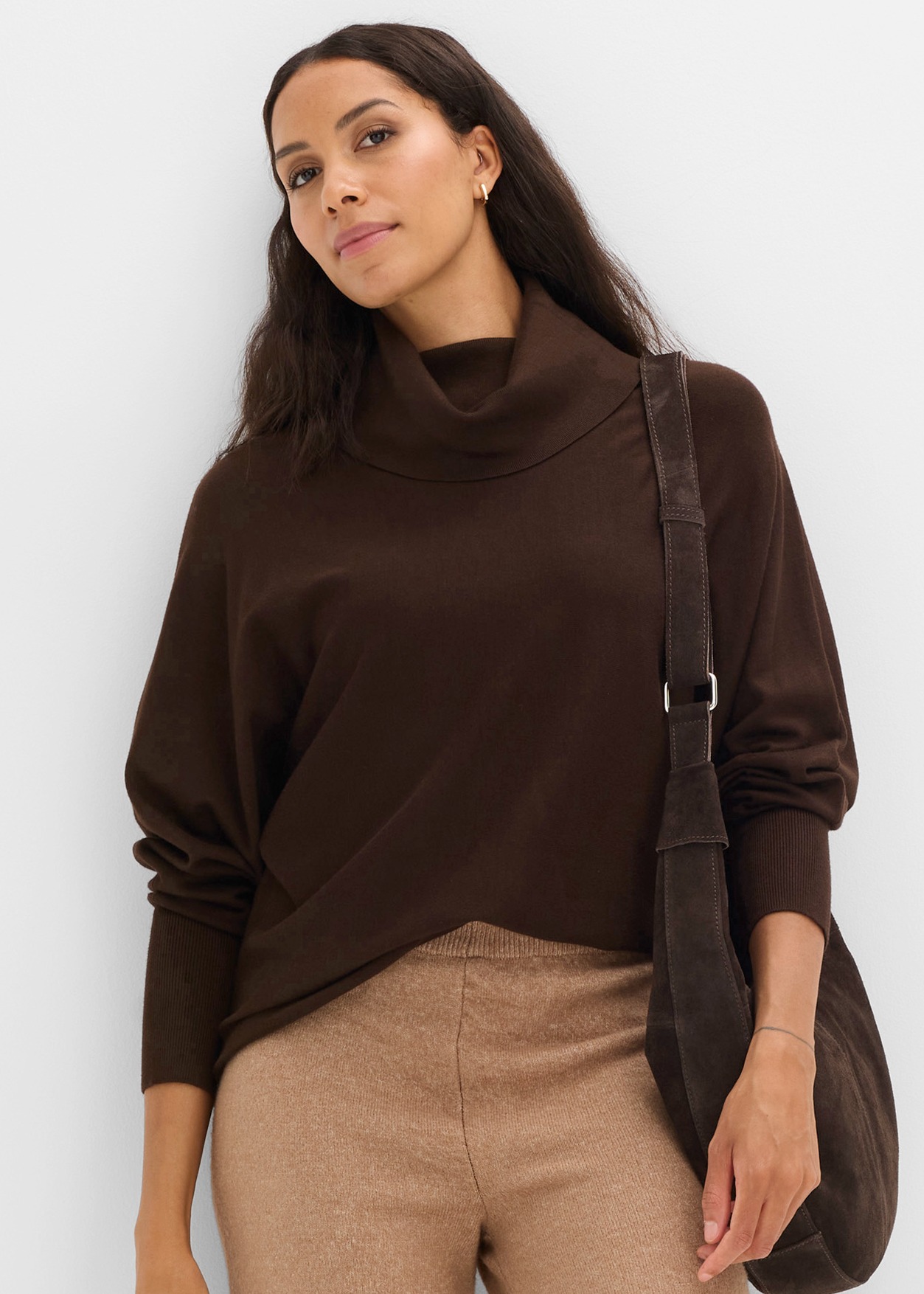 Dunkelbrauner Wasserfallkragen-Pullover und beigefarbene Hose mit passender Umhängetasche.