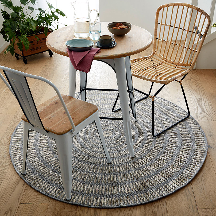 Gemütliches Interieur mit rundem Teppich, Holztisch und Stühlen in natürlichen Farbtönen.