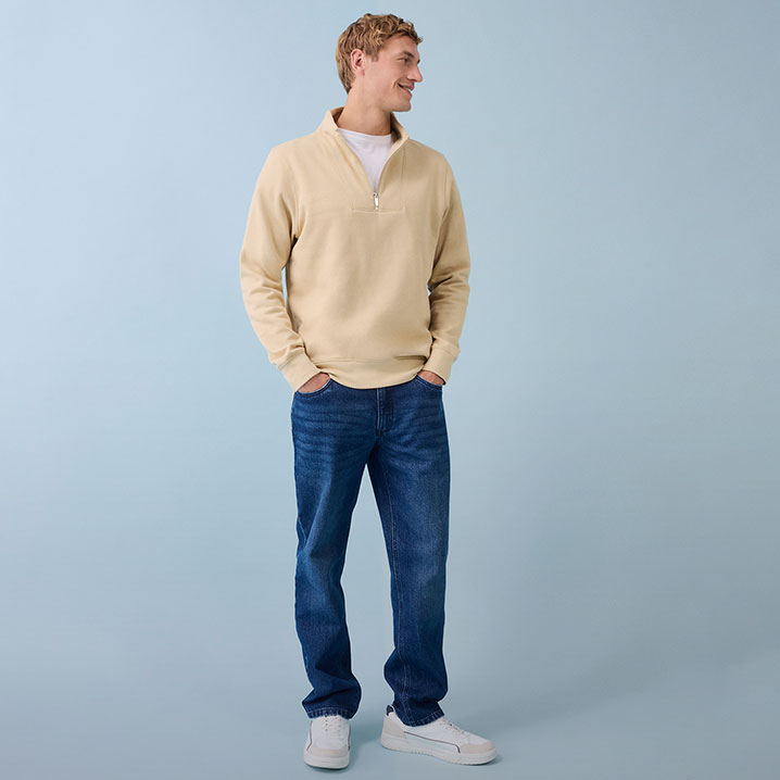 Beiger Pullover mit Reißverschluss, blaue Jeans und weiße Sneakers - lässiger Alltagslook für Männer.