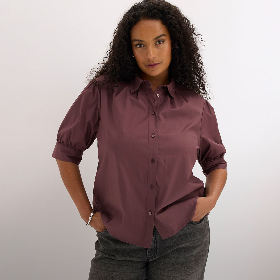 Bordeauxfarbene Bluse mit eleganten Puffärmeln und Kragen, dazu dunkle Jeans.