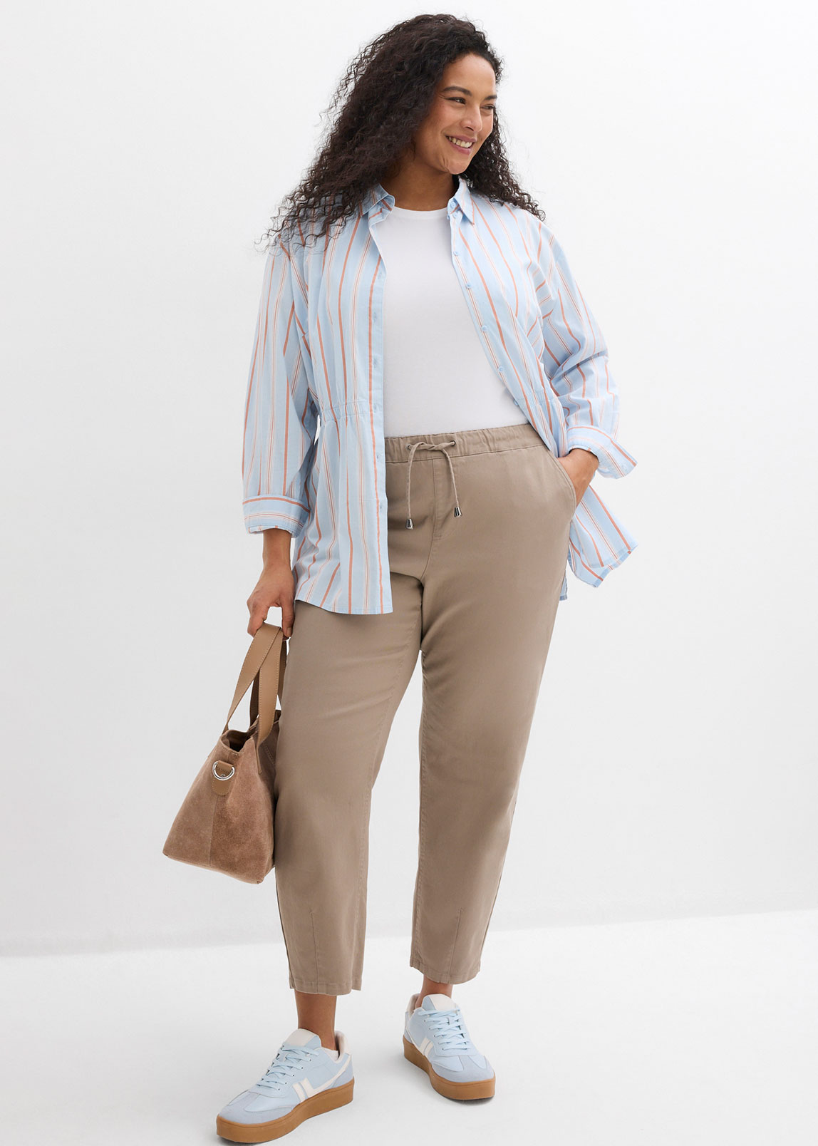 Gestreiftes Hemd über weißem T-Shirt, beige Hose und hellblaue Sneakers.