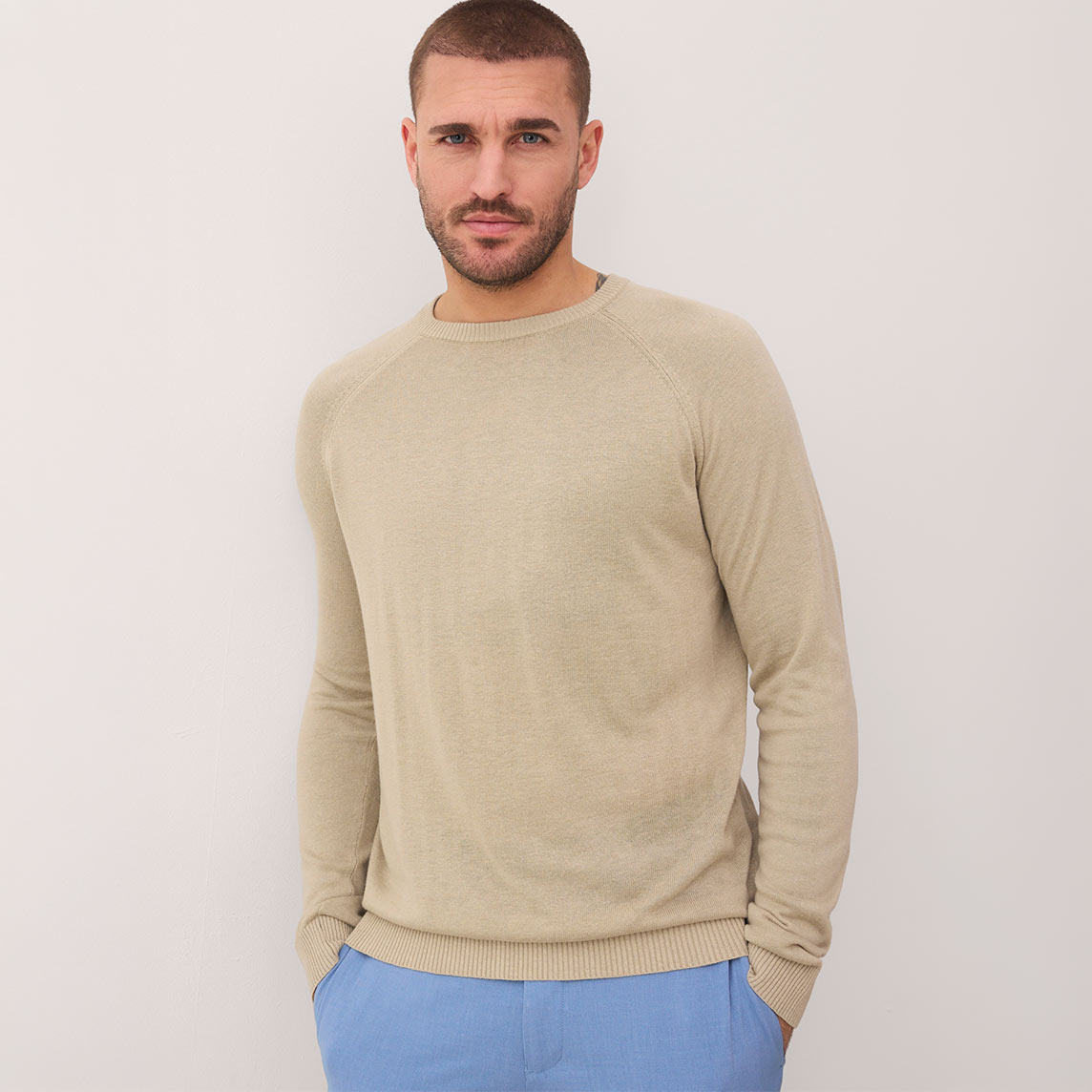 Mann trägt beigen Pullover und hellblaue Hose.