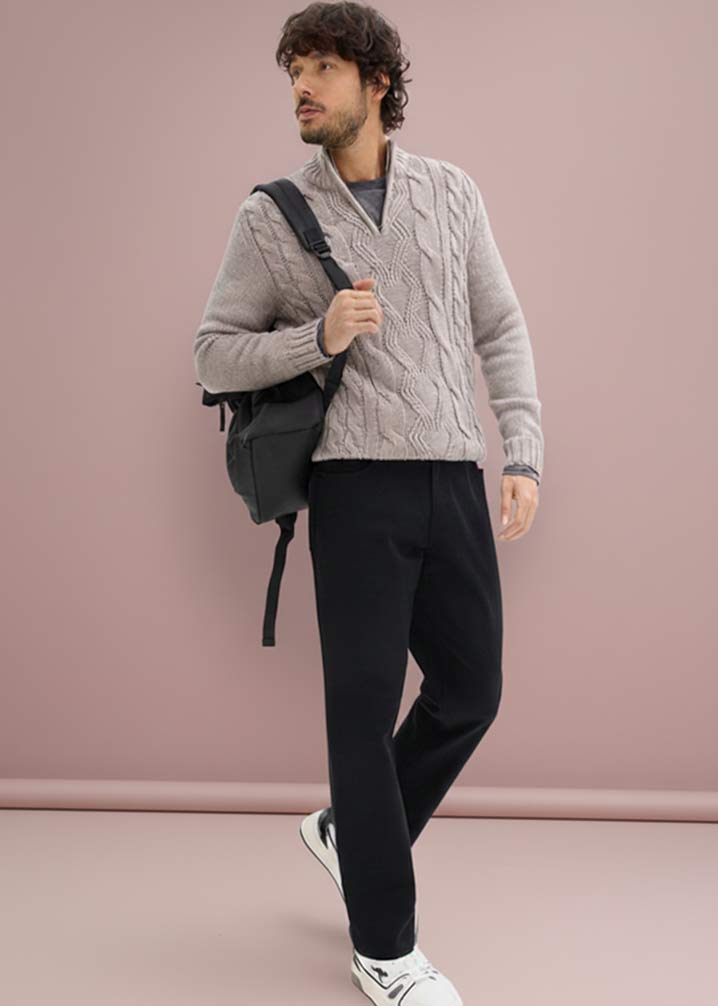 Ein beiger Strickpullover mit Zopfmuster, kombiniert mit dunkler Stretch-Hose.