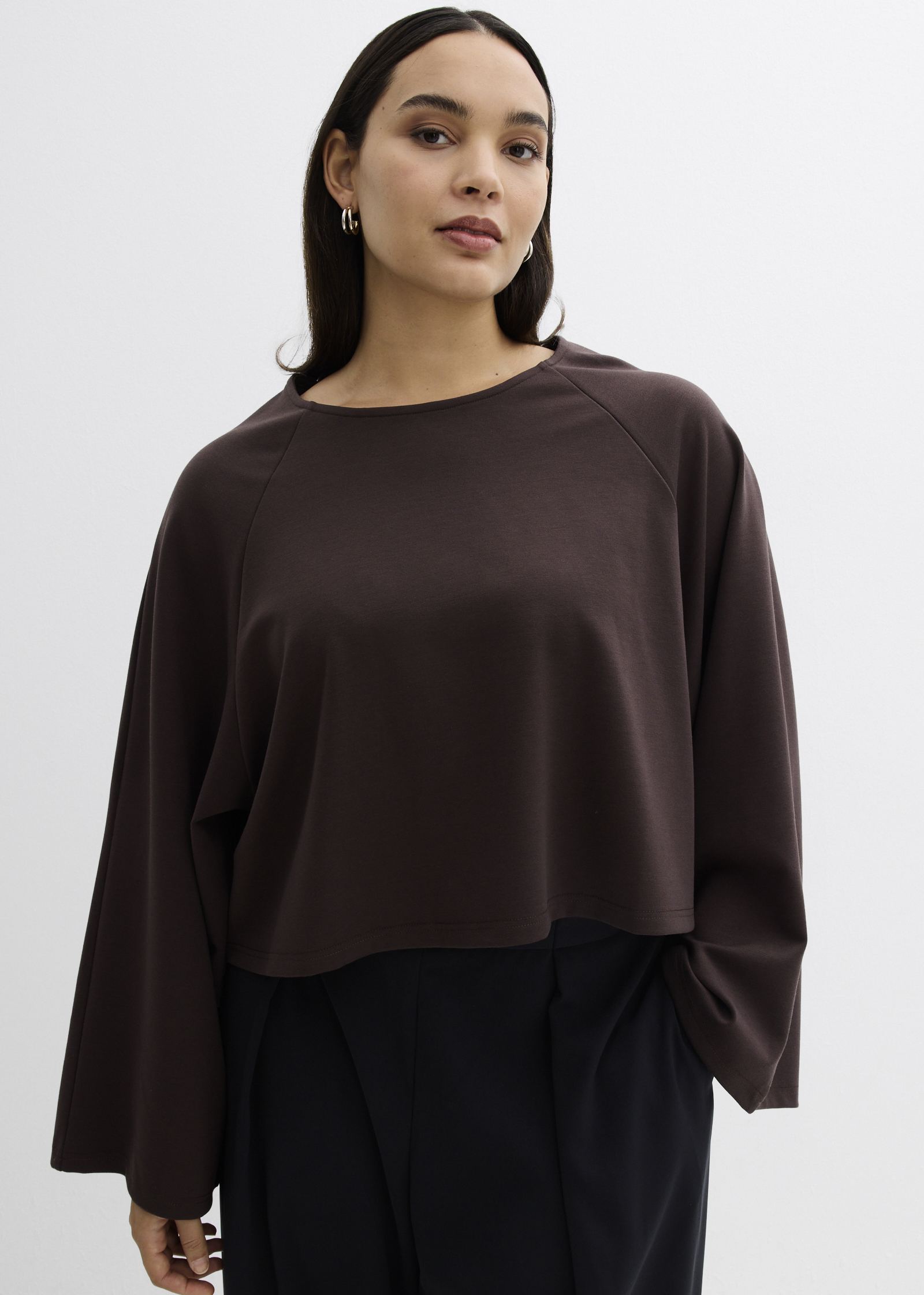 Dunkelbraunes Langarmshirt mit weiten Ärmeln und einer eleganten schwarzen Hose.