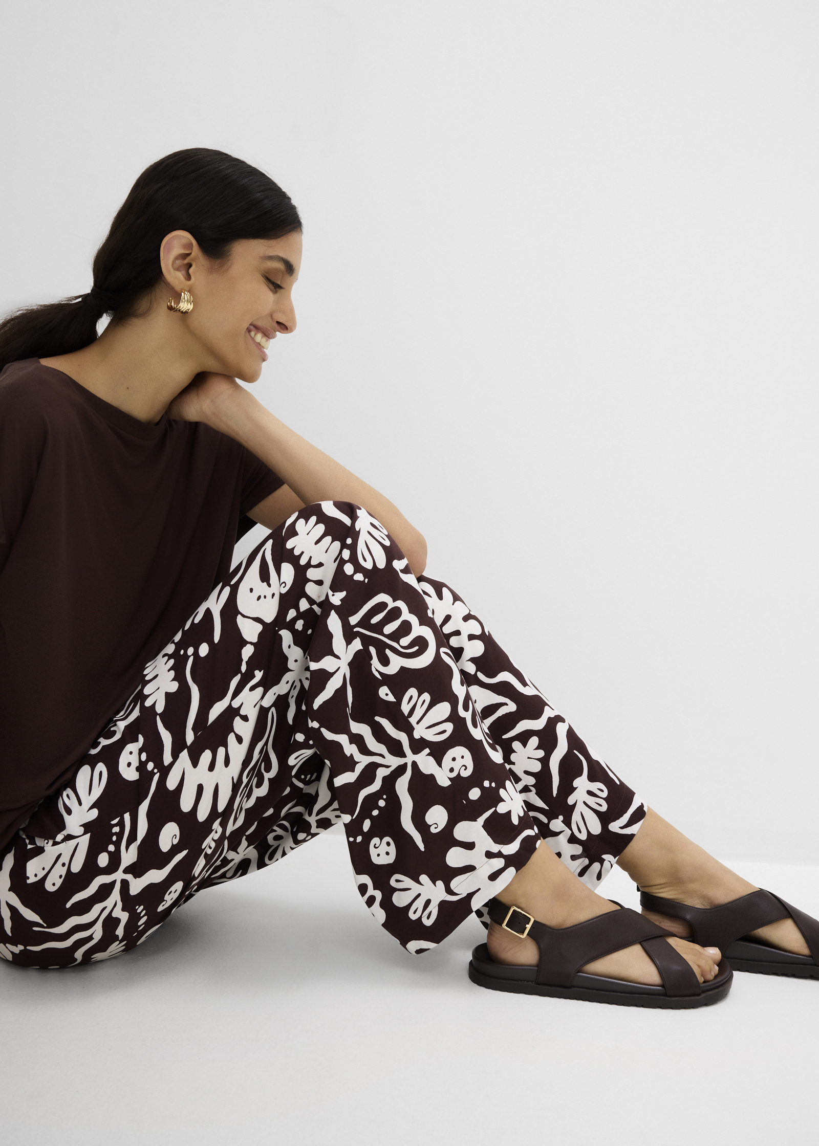 Braunes Oberteil, gemusterte Hose und bequeme dunkle Sandalen für einen entspannten Look.