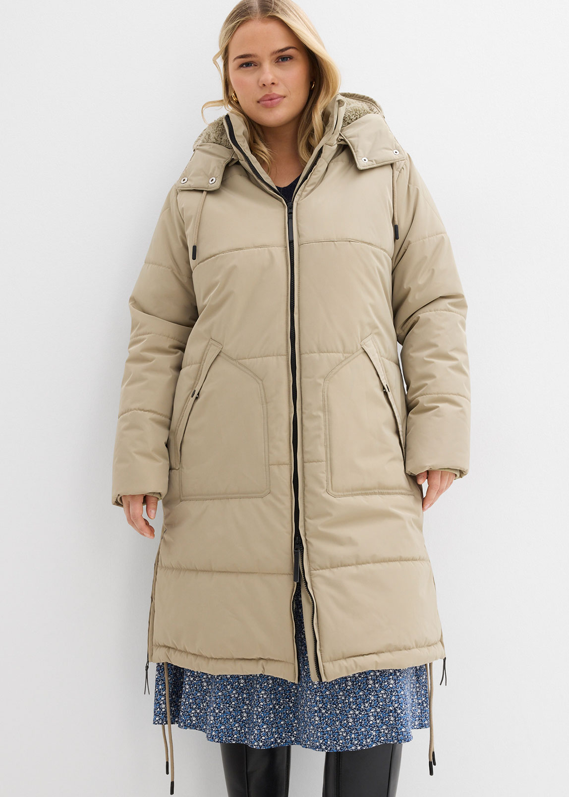 Beiger Steppmantel mit Kapuze über blauem Blumenkleid. 