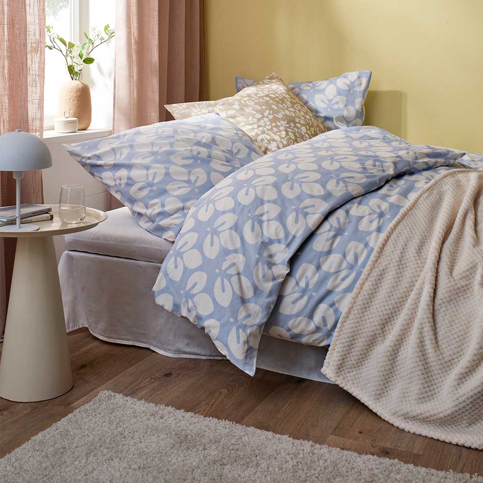 Bettwäsche in Blau und Weiß, beige Decke und rosa Vorhänge.