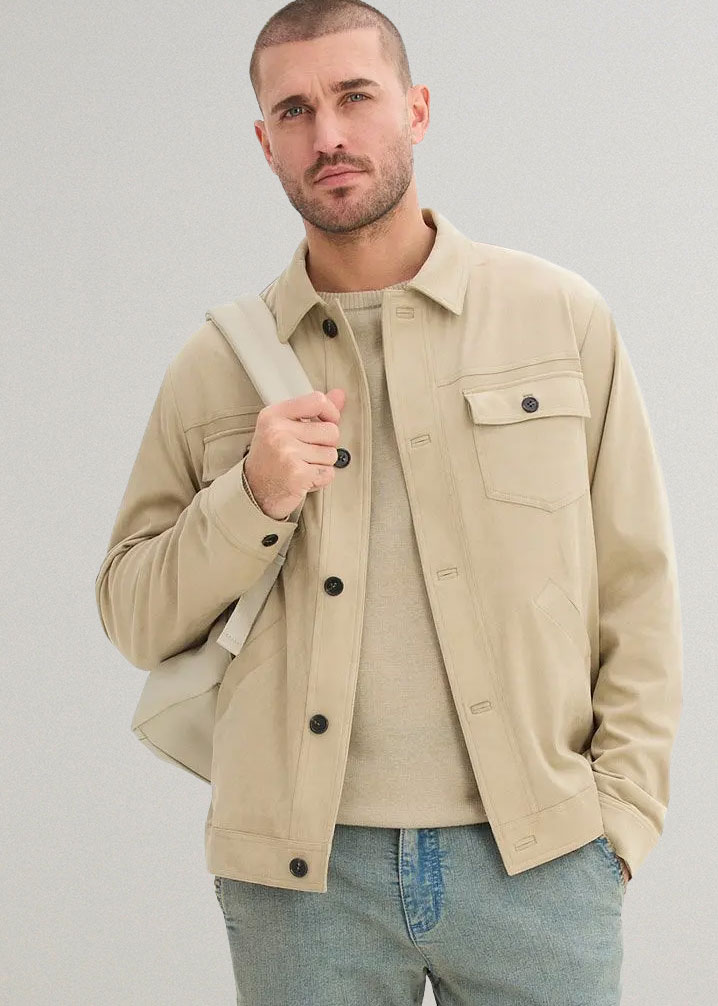 Beige Jacke über hellem Pullover, dazu Jeans und eine beigefarbene Tasche.