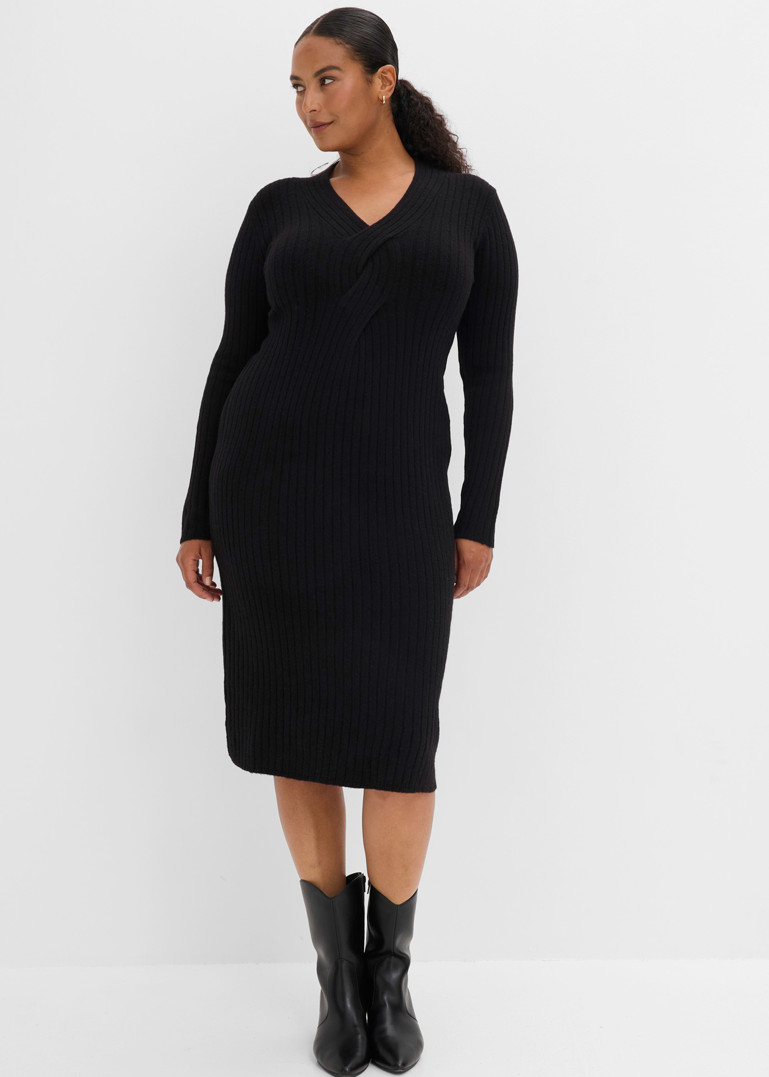 Eine Frau trägt ein elegantes schwarzes, geripptes Strickkleid und schwarze Stiefel.