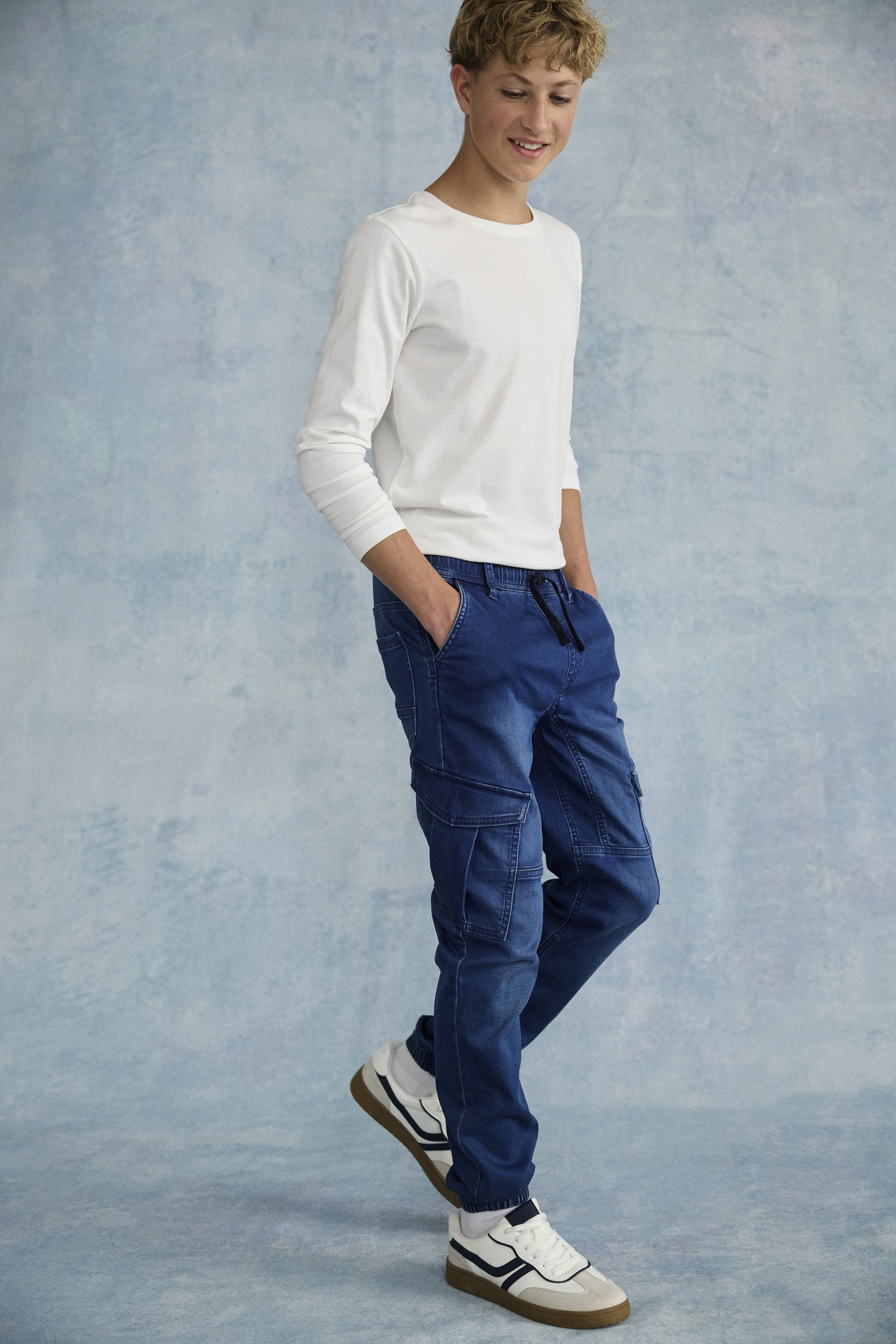 Lässiger Look: Weißes Langarmshirt kombiniert mit blauen Cargo-Jeans und weißen Sneakern.