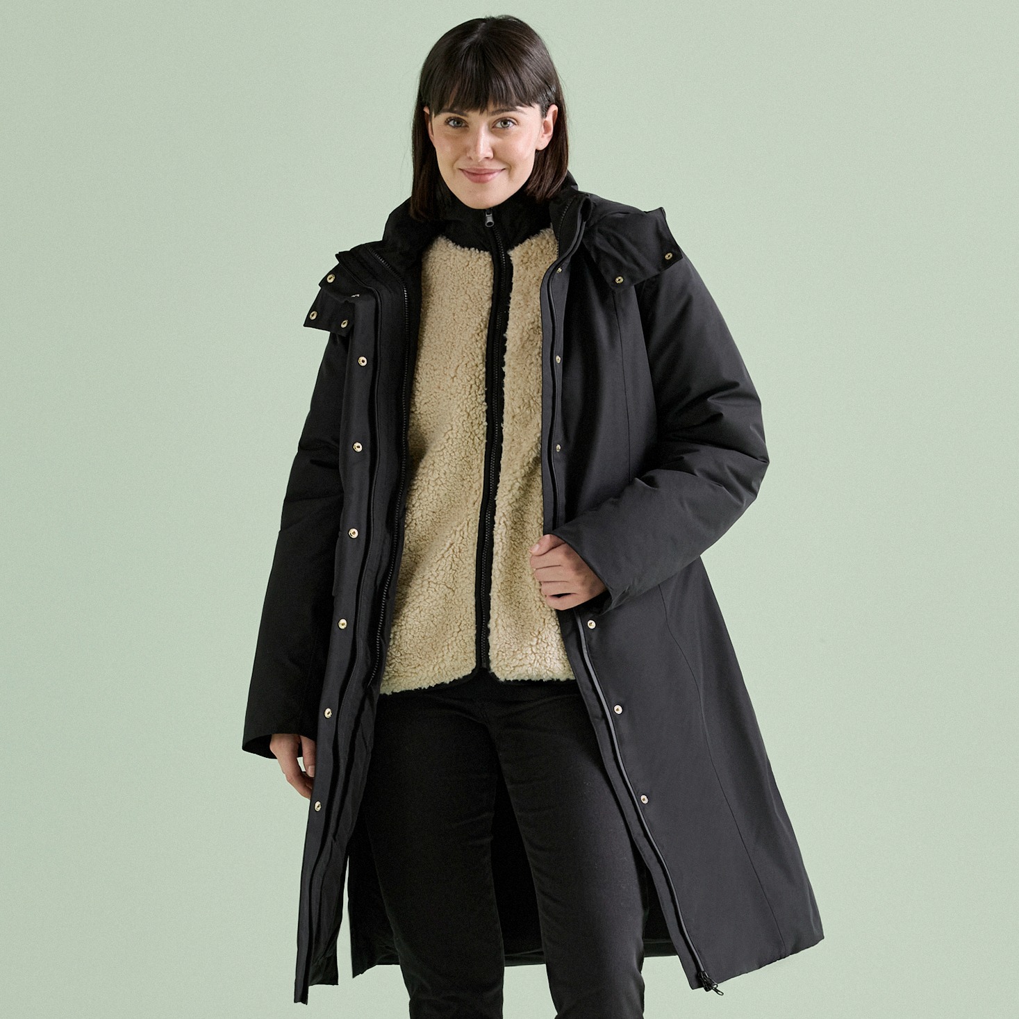 Warmer schwarzer Mantel über beiger Fleecejacke und dunkler Hose.