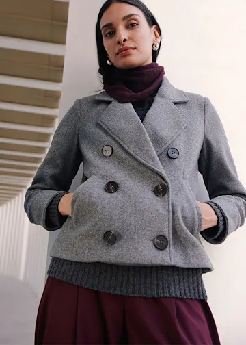 Grauer Kurzmantel, dunkler Rollkragenpullover und weinrote Hose.