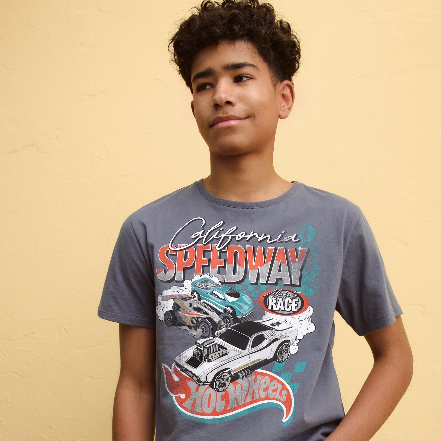 Junge trägt ein graues T-Shirt mit buntem Autorennen-Motiv und Speedway-Aufdruck.
