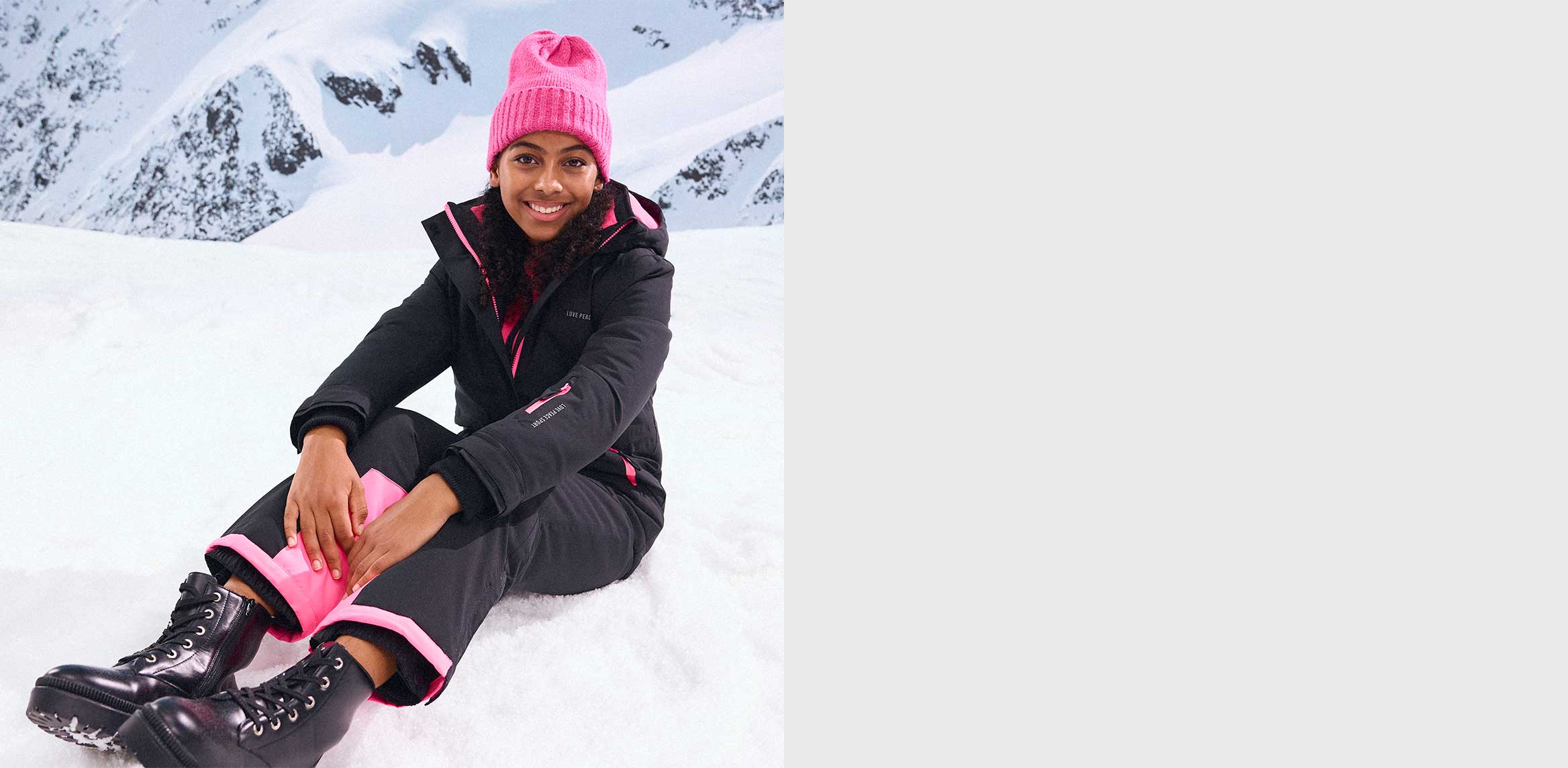 Schwarze Winterjacke und Hose, pinke Mütze.