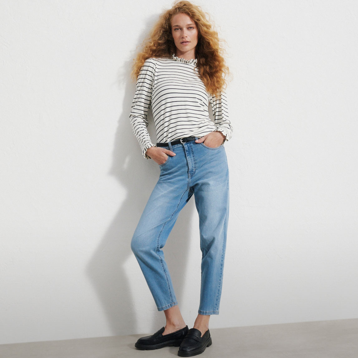 Gestreiftes Langarmshirt, helle High-Waist-Jeans, schwarzer Gürtel und Loafer.