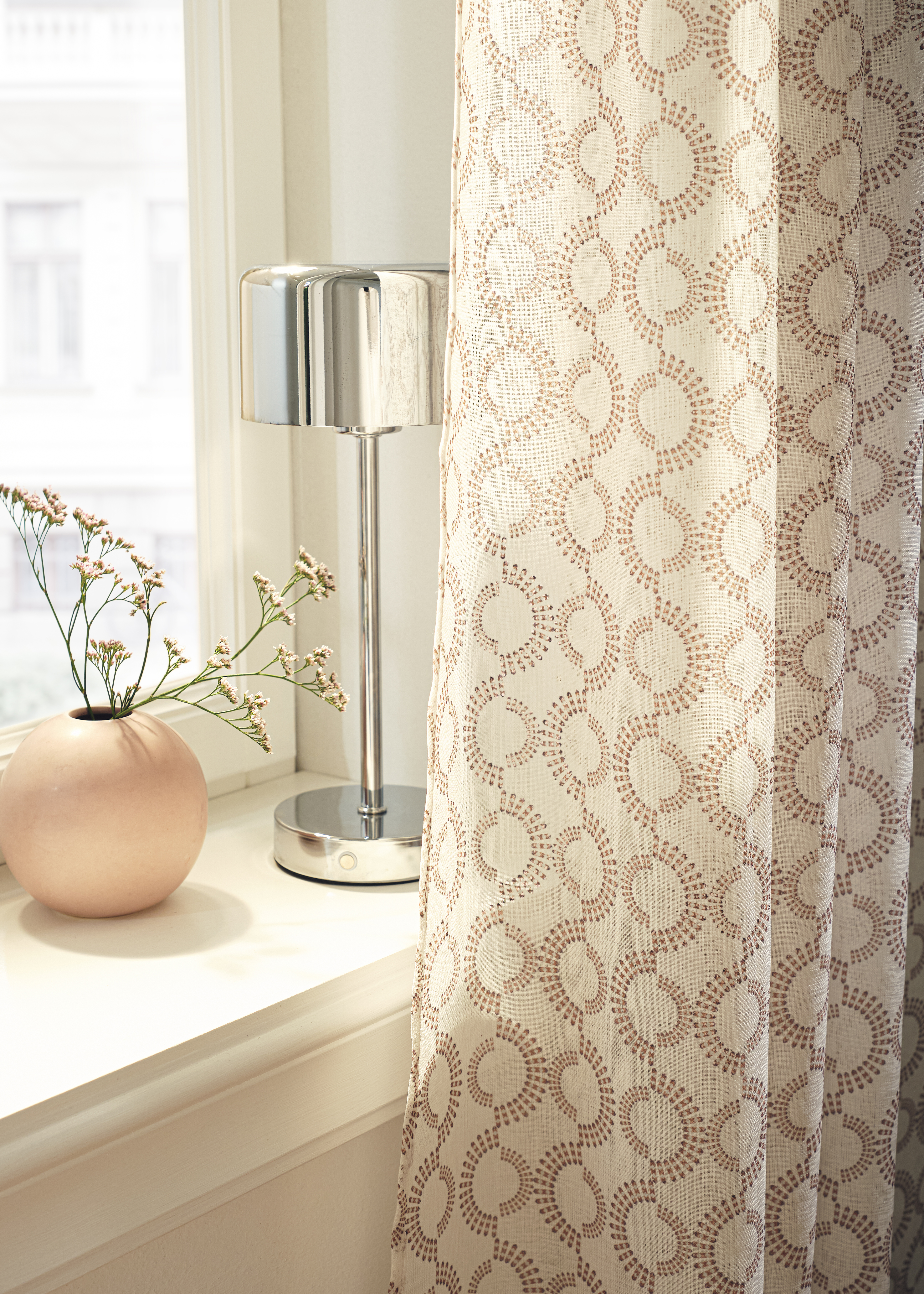 Dekorativer Vorhang mit Kreismuster, Vase mit Blumen und moderne Lampe auf der Fensterbank.