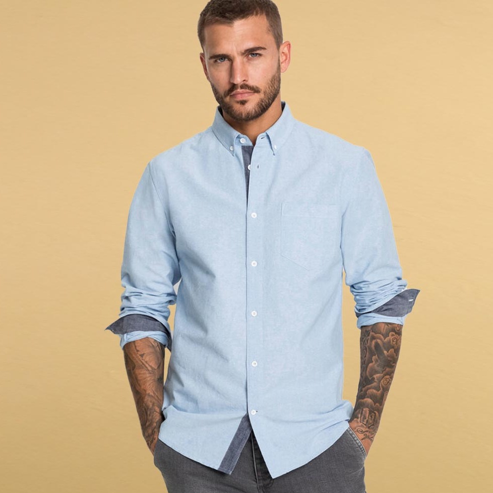 Hellblaues Button-Down-Hemd, aufgekrempelte Ärmel, graue Jeans. Lässiger, aber gepflegter Look für den Alltag.