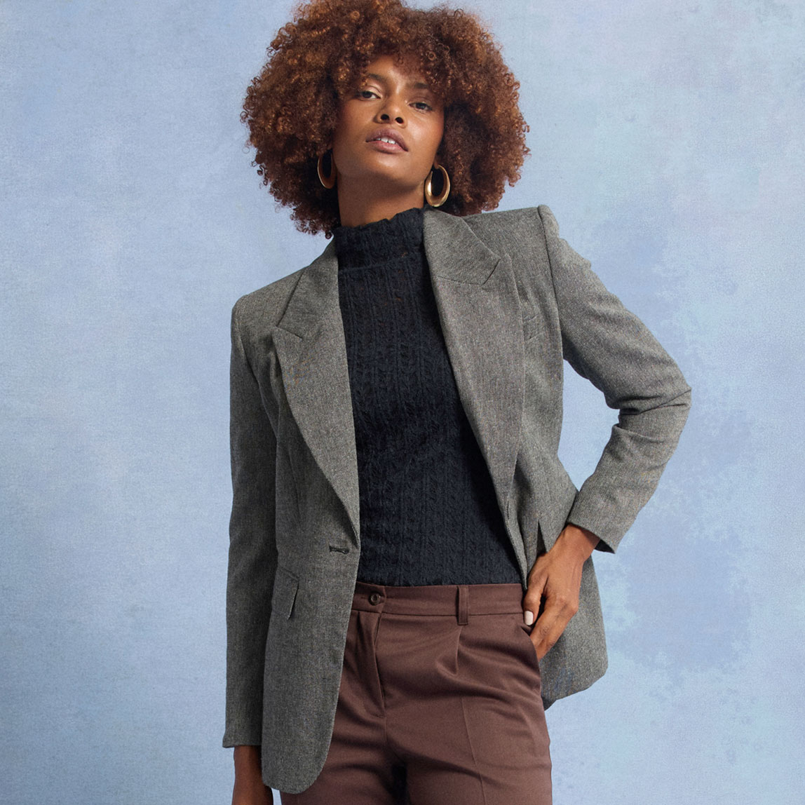 Grauer Blazer über dunklem Rollkragenpullover, kombiniert mit brauner Hose.